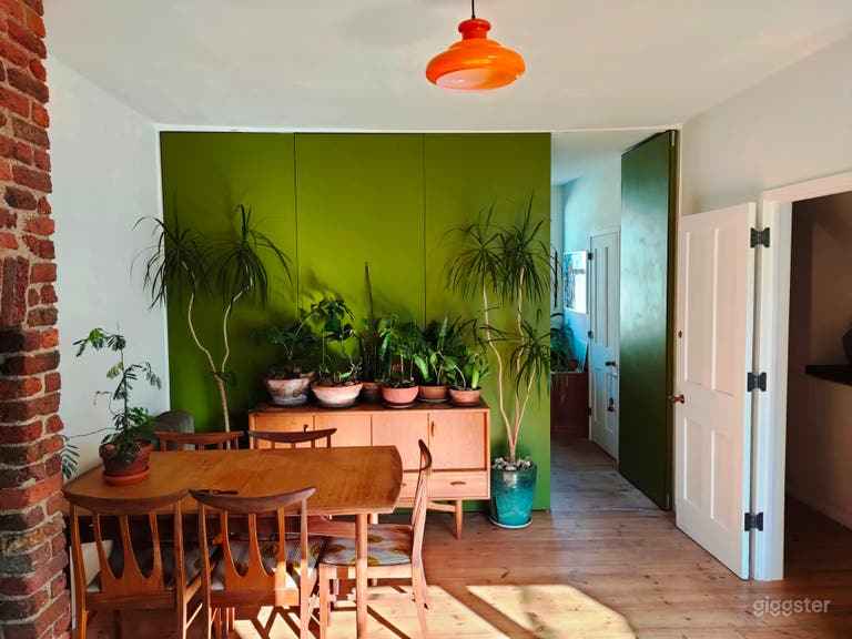  Dining area with mid century dining table and chairs and sideboard. Green folding wall leads to double bedroom behind. 