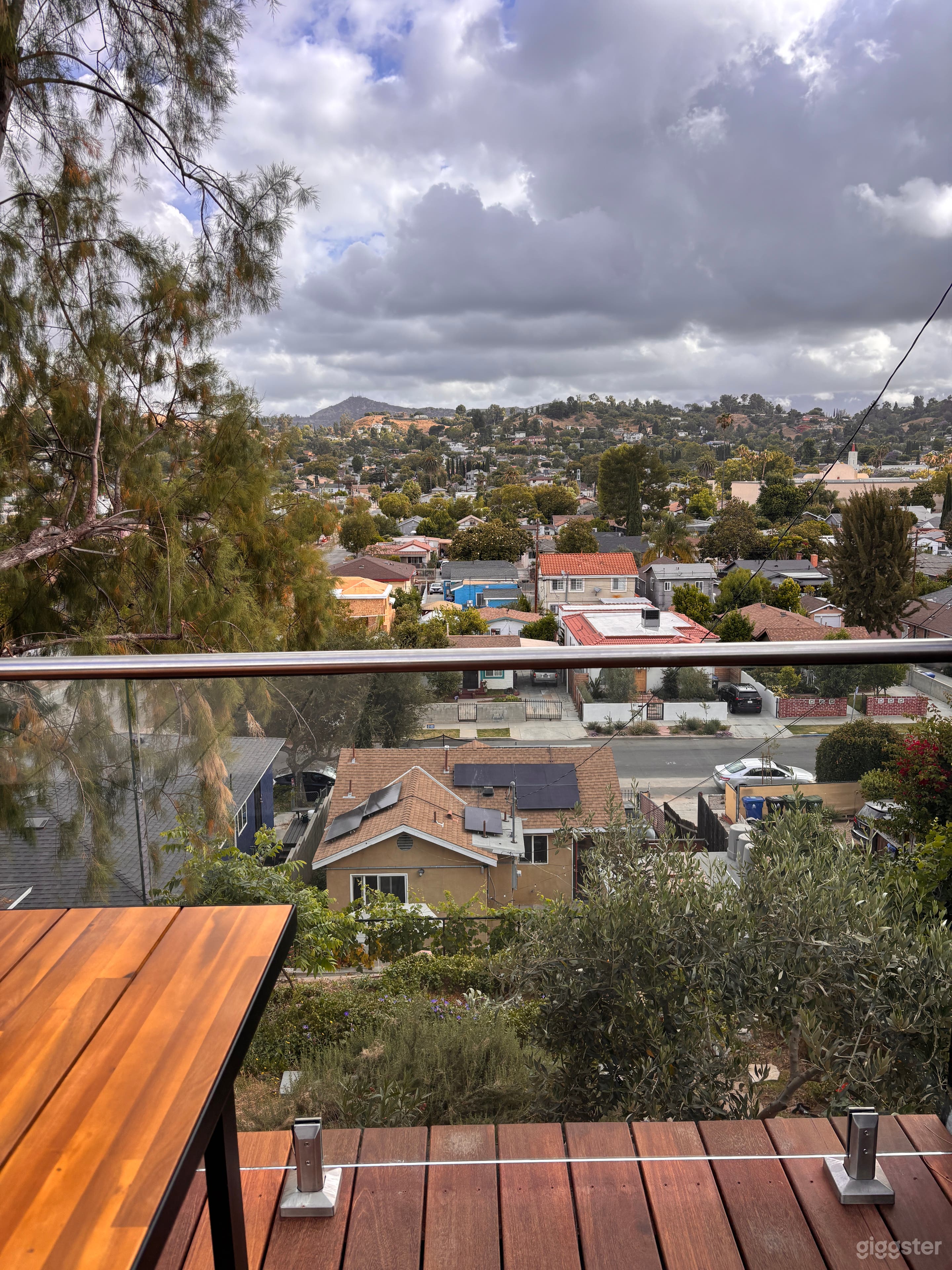 Rooftop deck with glass railing, warm wood decking, lush hillside surroundings, and magnificent Los Angeles views—perfect for exterior scenes, golden-hour photo shoots, lifestyle content, brand campaigns, and intimate creative moments.