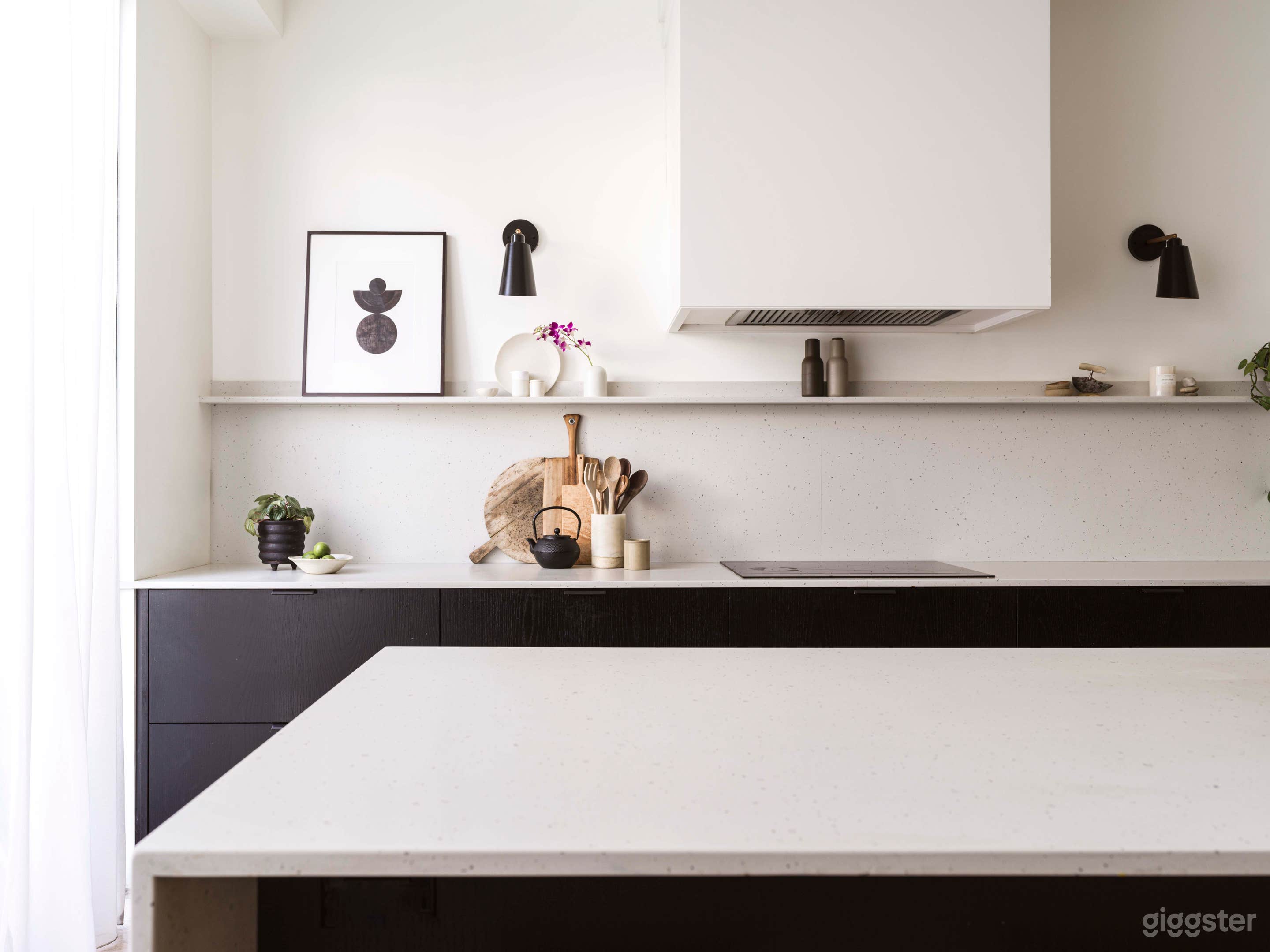 Light filled modern open plan Kitchen &amp; Island with stained black cabinetry, hidden pantry and appliances. White oak floor and furnishings. Large back doors open to the backyard.