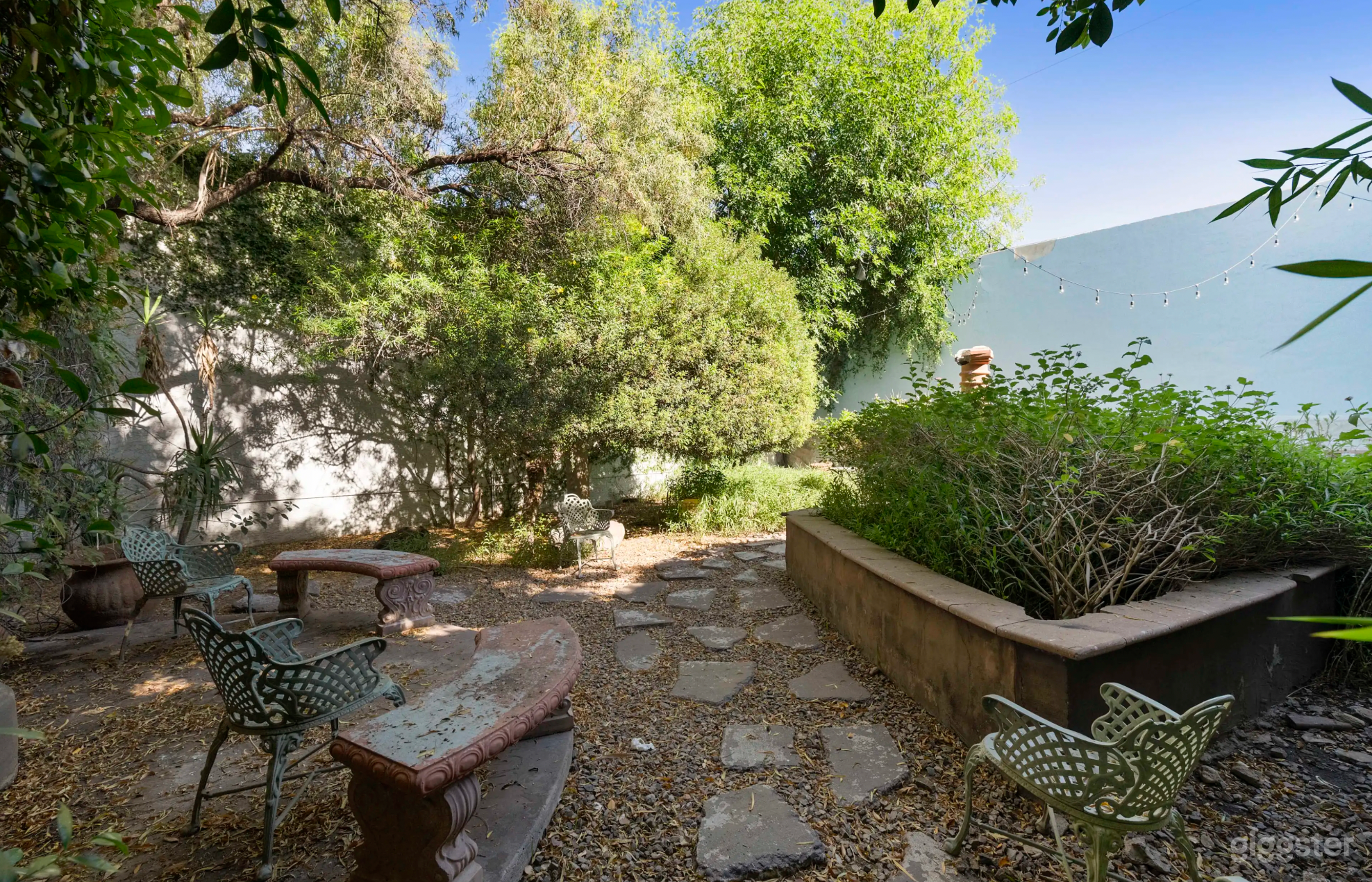 Oasis | Outdoor Studio Space: Lush greenery, rustic accents, stone pathways, string lights, versatile layouts for various shoots.