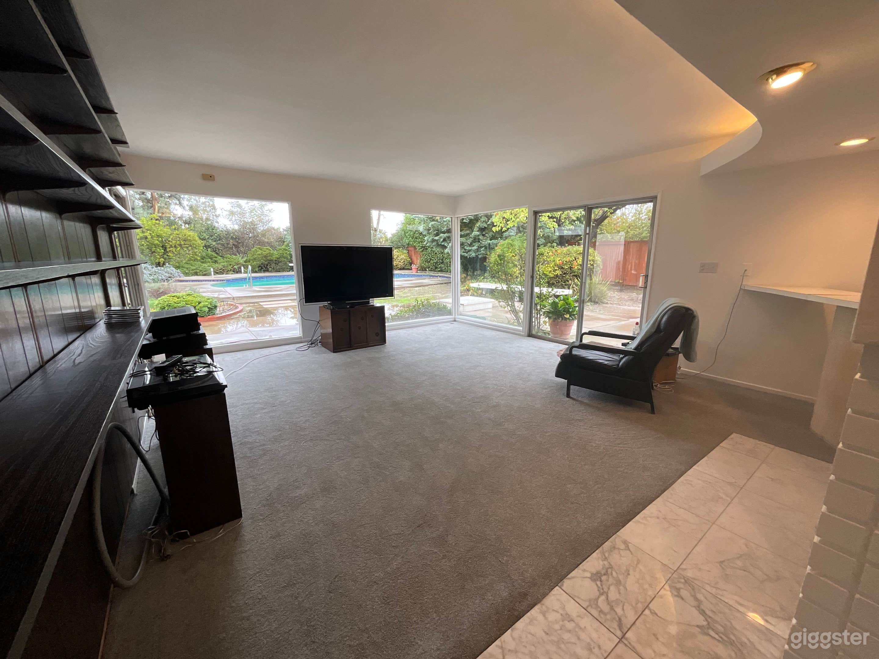 Living room with bar, large glass windows to the back yard. Mid century style. 