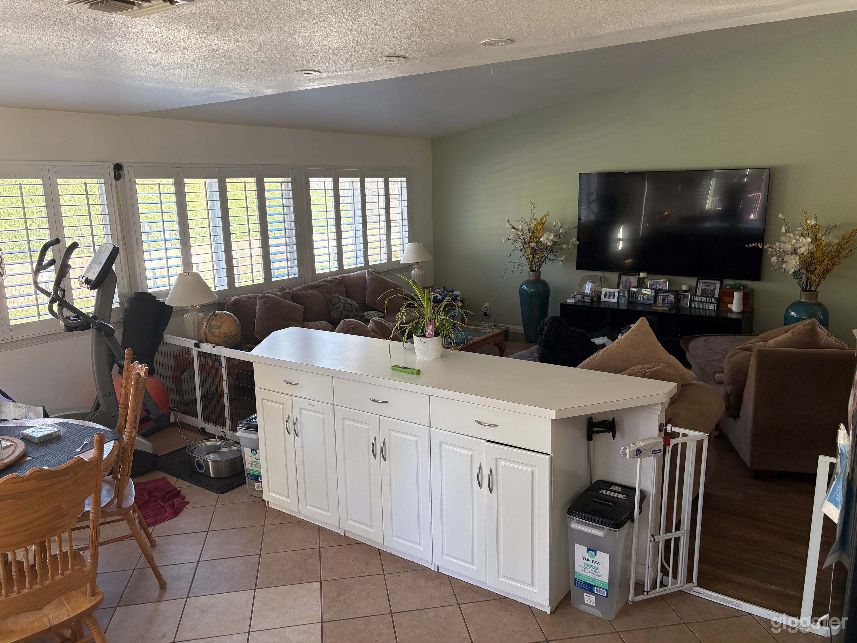 Open white kitchen with center island.  White dog gates are removable. Living room includes an 85 inch TV, stereo and DVD. Dining room includes elliptical.