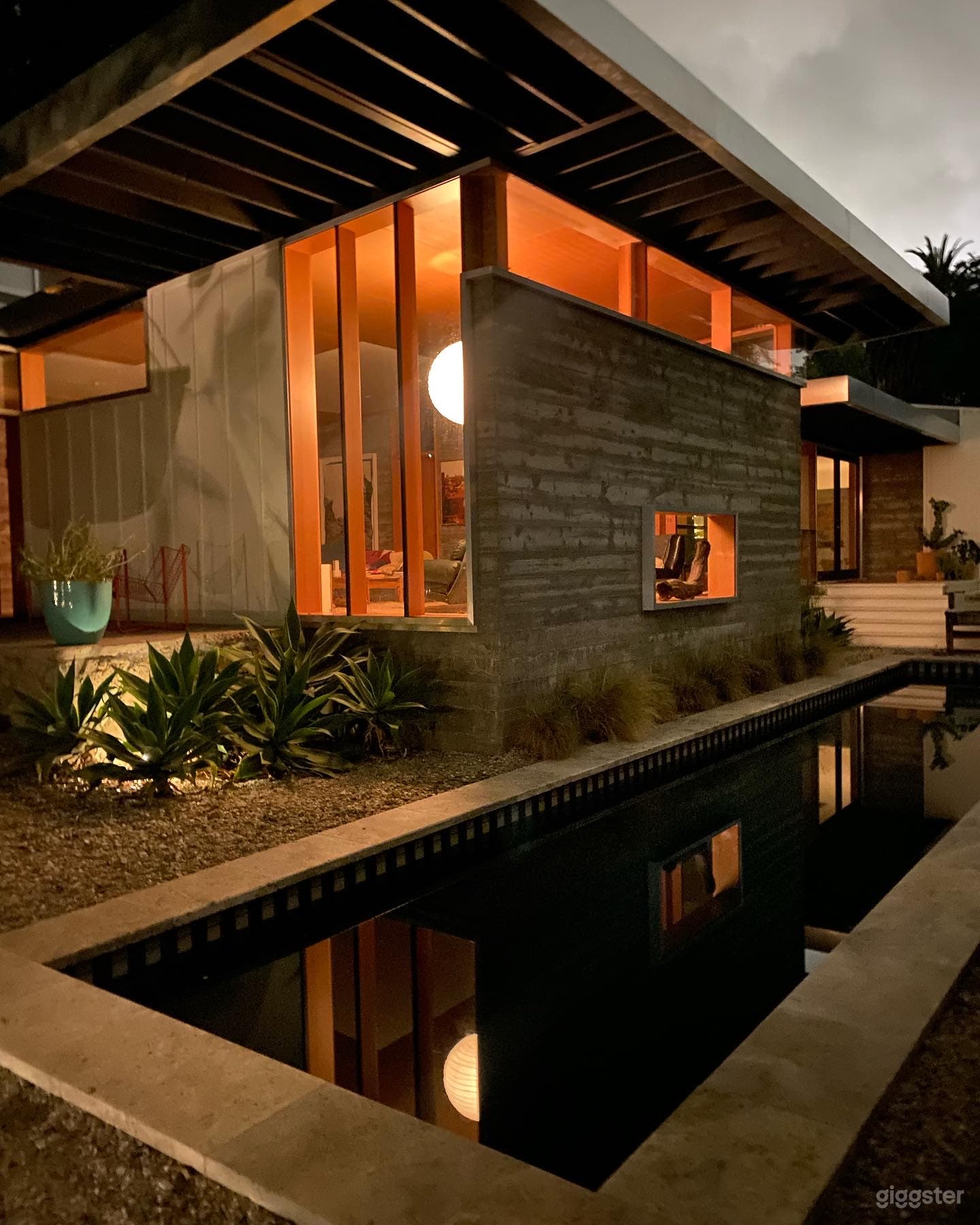 View of the front of the house from the front yard with the lights on reflecting in pool. 