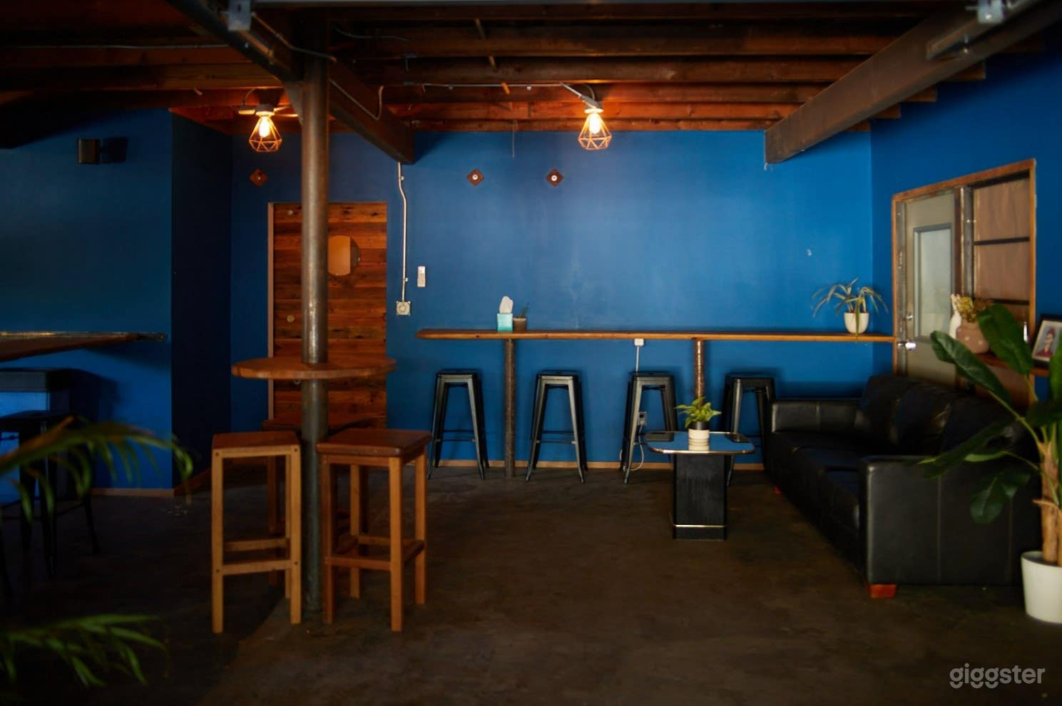 Black leather couch and bar seating, exposed wood and metal beams.