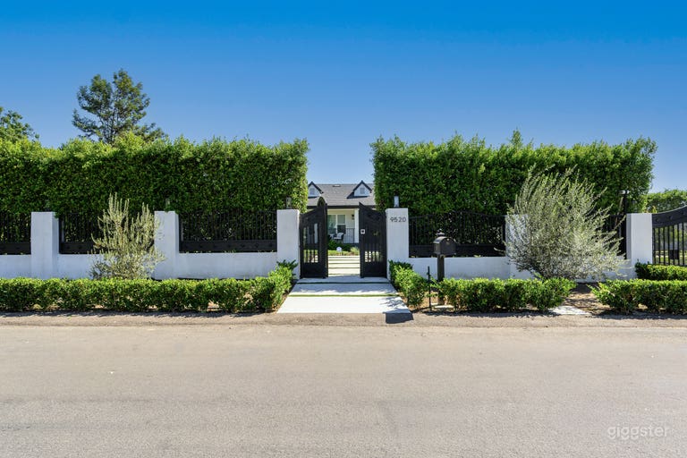  Elegant street view featuring a gated entrance with stately columns and lush ficus-covered walls, offering a private and sophisticated curb appeal. 
