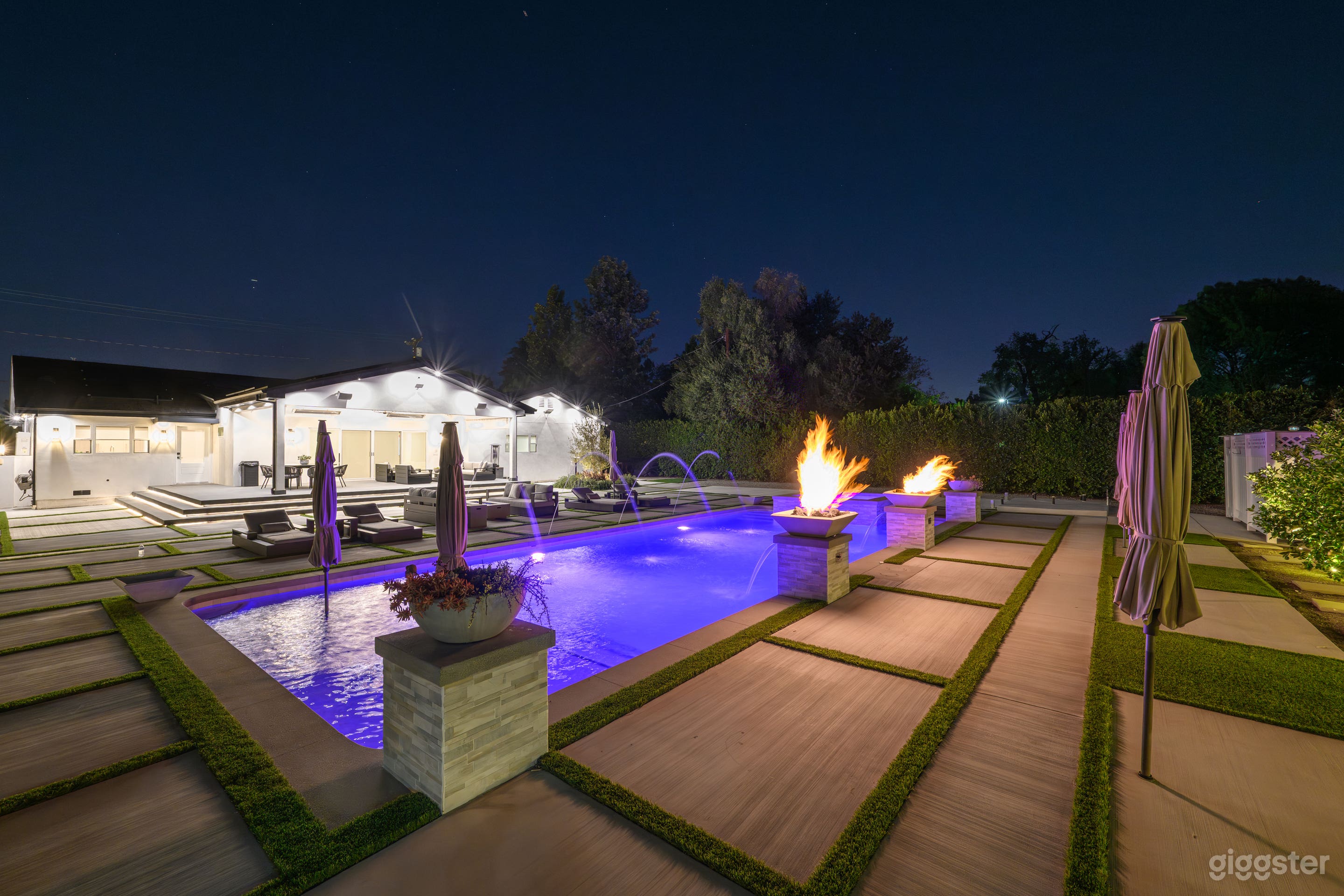 Pool at night featuring glowing fire bowls, flowing fountains, and ambient lighting, creating a striking and luxurious outdoor atmosphere.