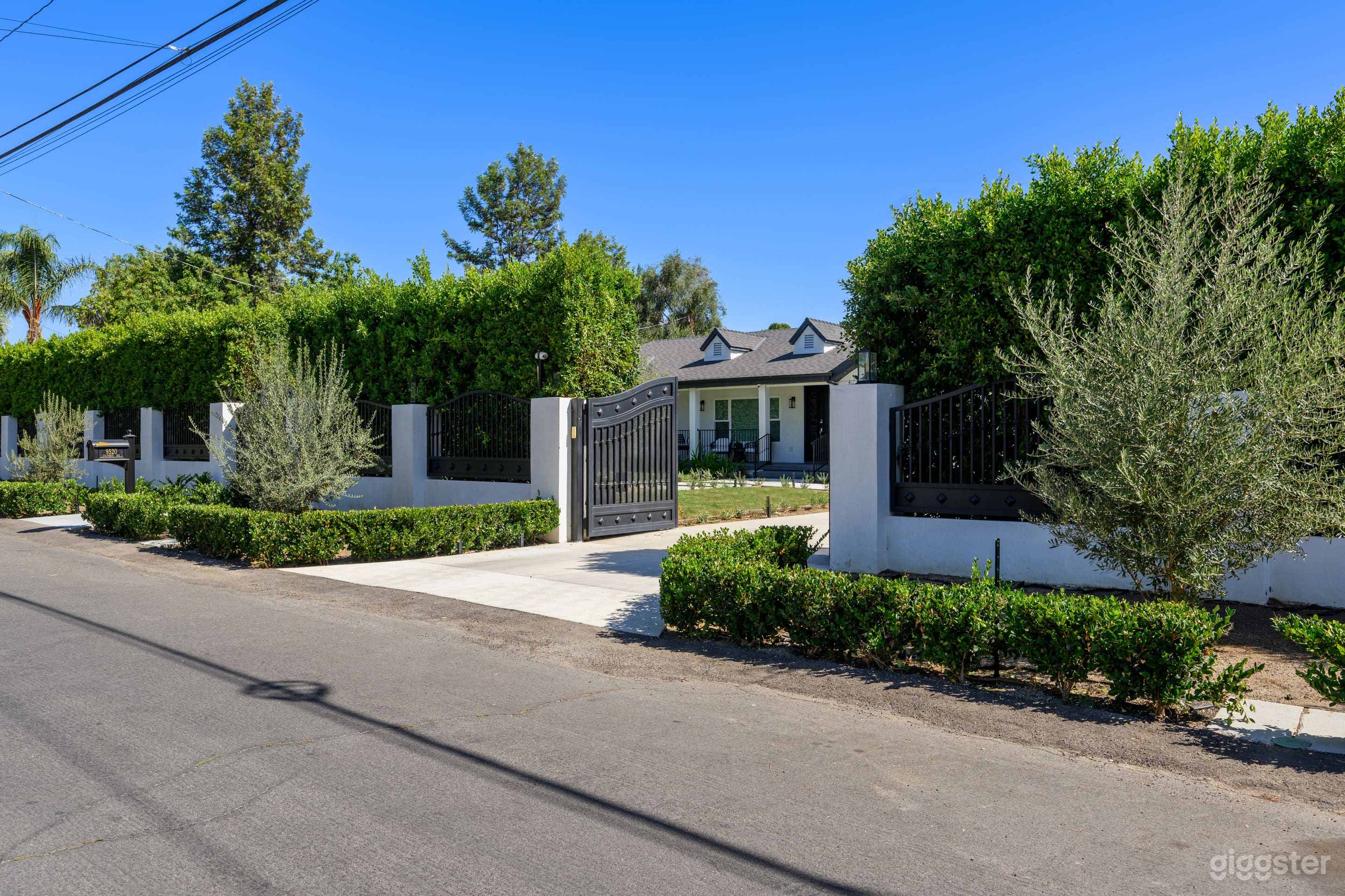 Elegant street view featuring a gated entrance with stately columns and lush ficus-covered walls, offering a private and sophisticated curb appeal.