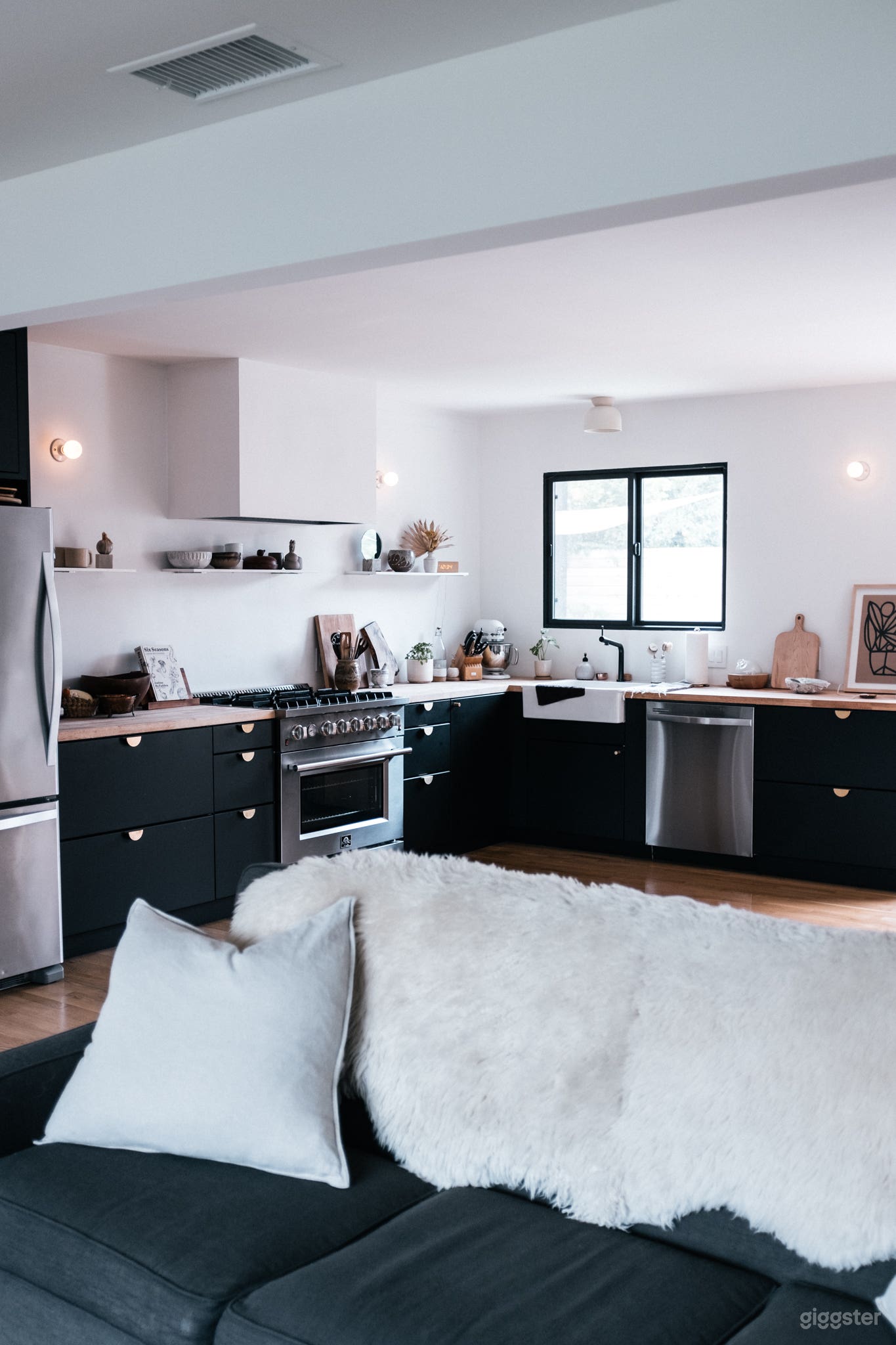 Open kitchen with matte black lower cabinets, light butcher block counter tops and custom plaster range hood.