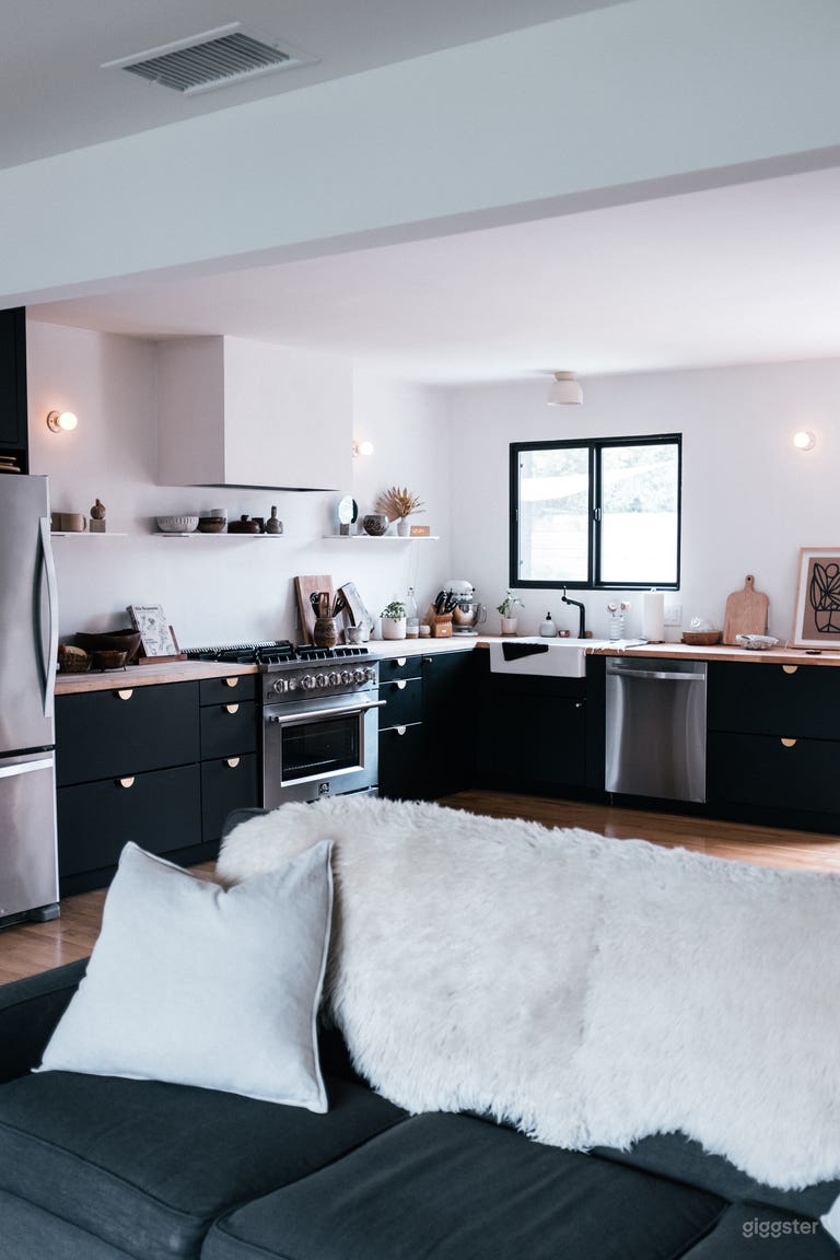  Open kitchen with matte black lower cabinets, light butcher block counter tops and custom plaster range hood. 