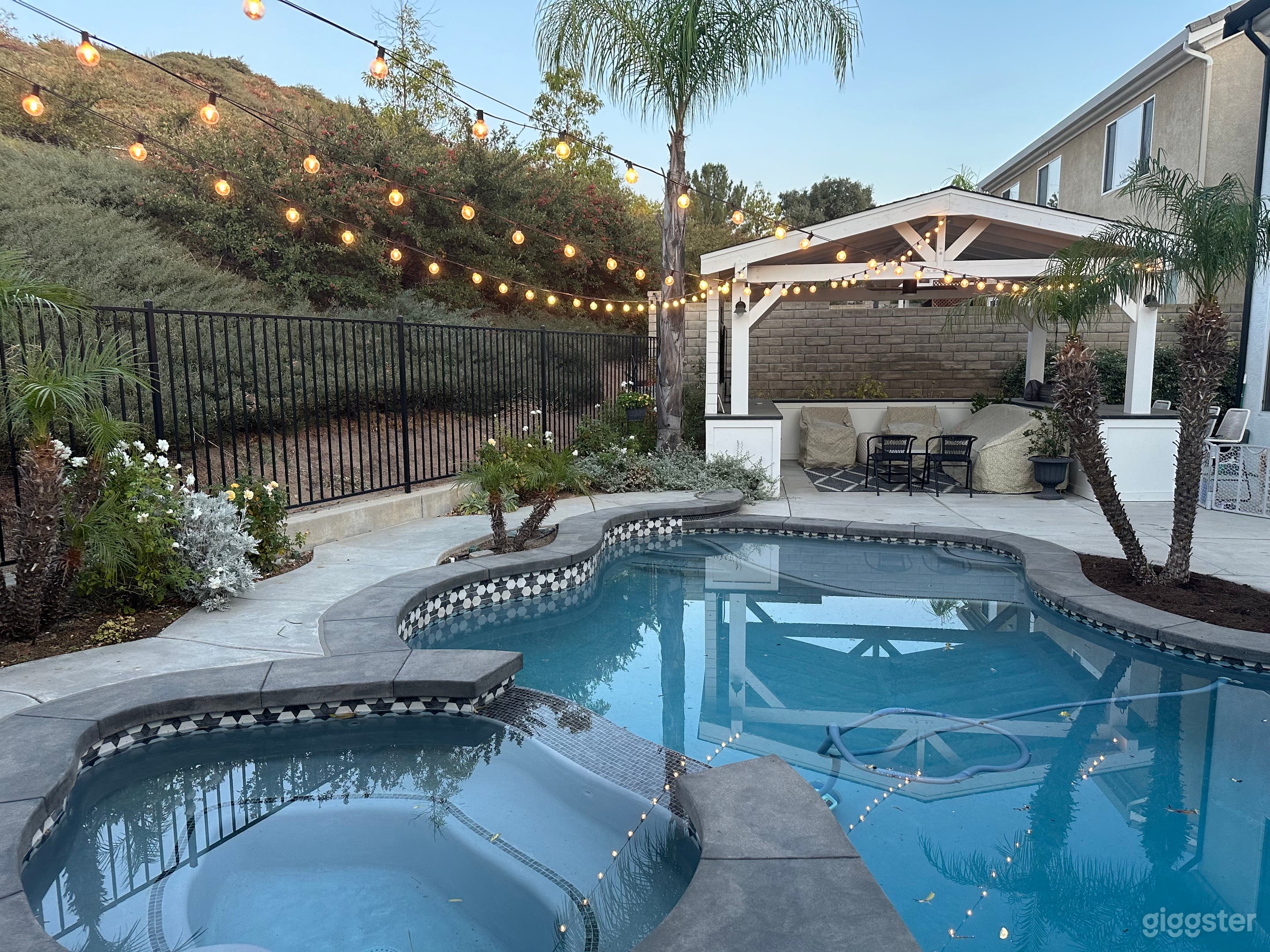 Beautifully remodeled pool looking back toward outdoor room with farmhouse style / board and batten look with couches, TV, built in grill, counter with 4 stools.