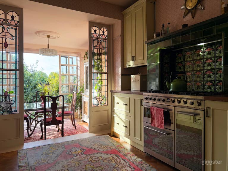  The kitchen has Edwardian stained glass panels, framing the dining area, green and pink tiled stove, a creamy-yellow vintage style kitchen with large nude pink crittall doors, leading to a patio area and large leafy garden. 