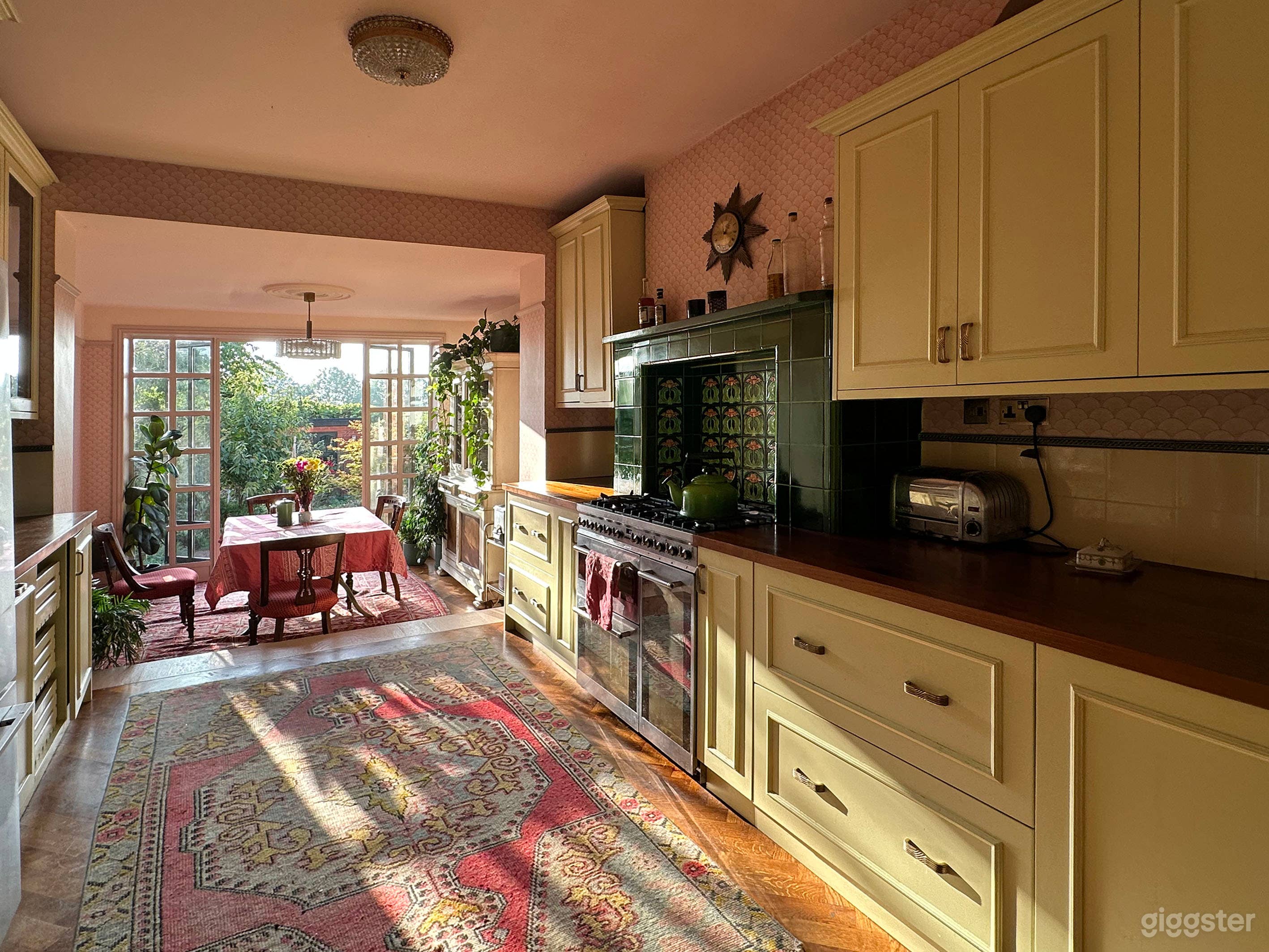 The kitchen has vintage green and pink tiles around the stove area, parquet wooden floor, cream cabinetry and dining area overlooking the garden.