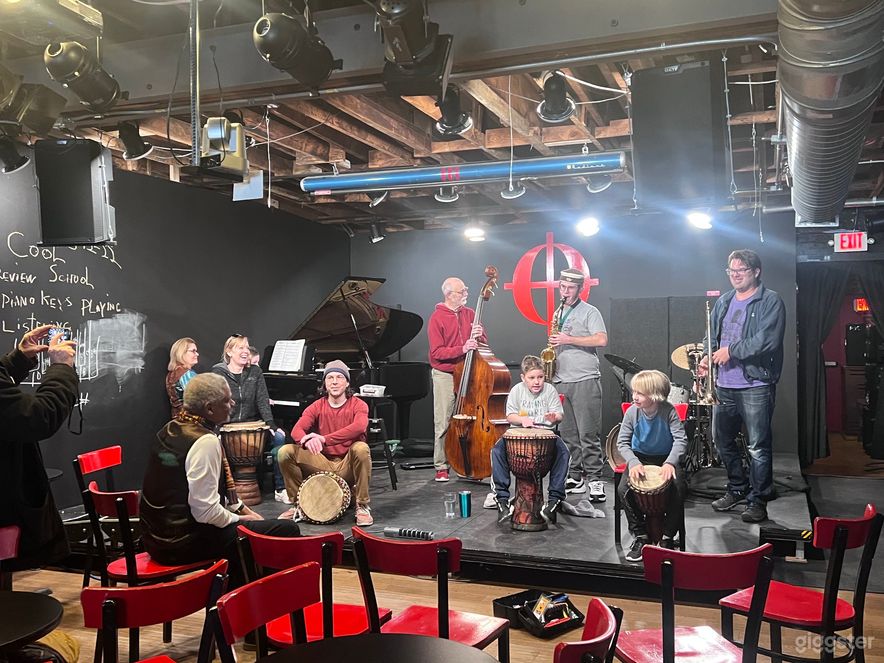 Weekly Cool School is in session. The wall next to the piano is a huge blackboard. There’s a projector and screen, sound system, and various instruments.