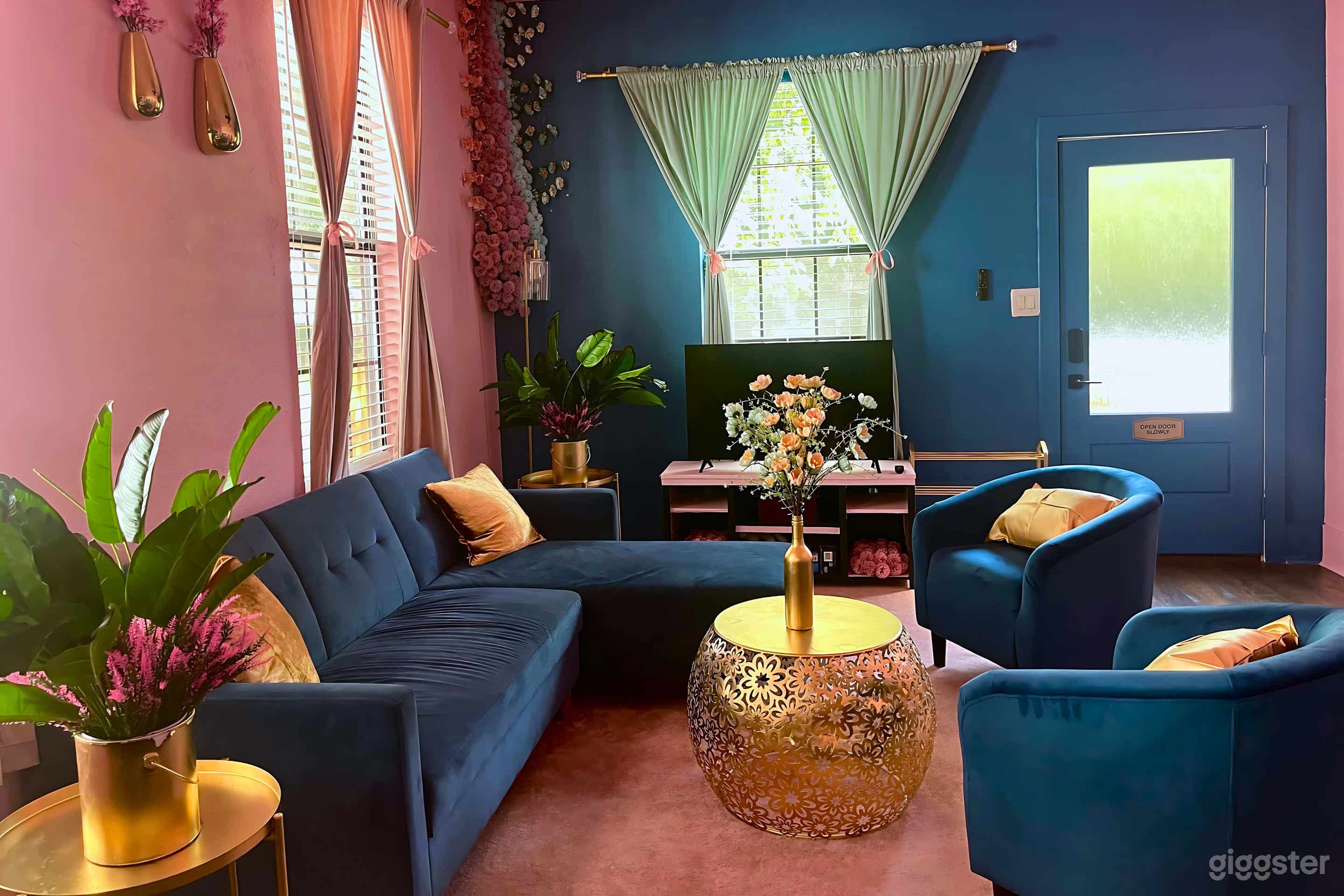 Charming living room with vibrant blue and blush pink tones, plush seating, gold accents, and lush greenery—a perfect blend of comfort and style.