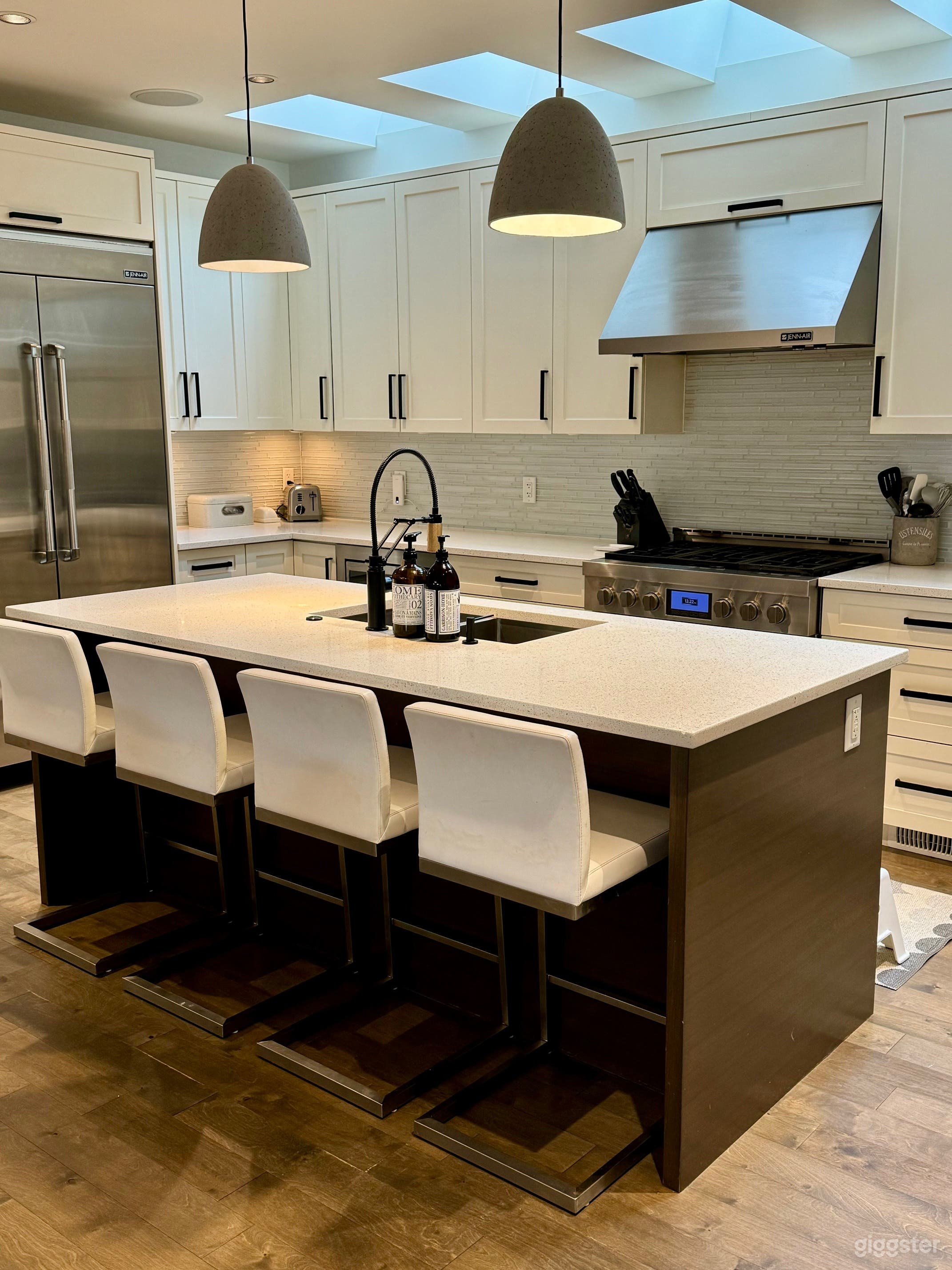 White kitchen with stainless steel appliances and silver pendant lights. Black accent.