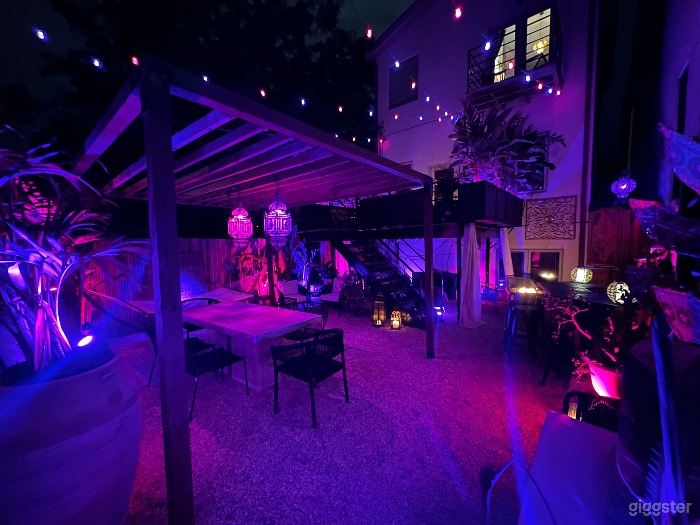Pea-gravel Spanish-inspired courtyard with timber pergola, embroidered parasols, lanterns, and dining table.