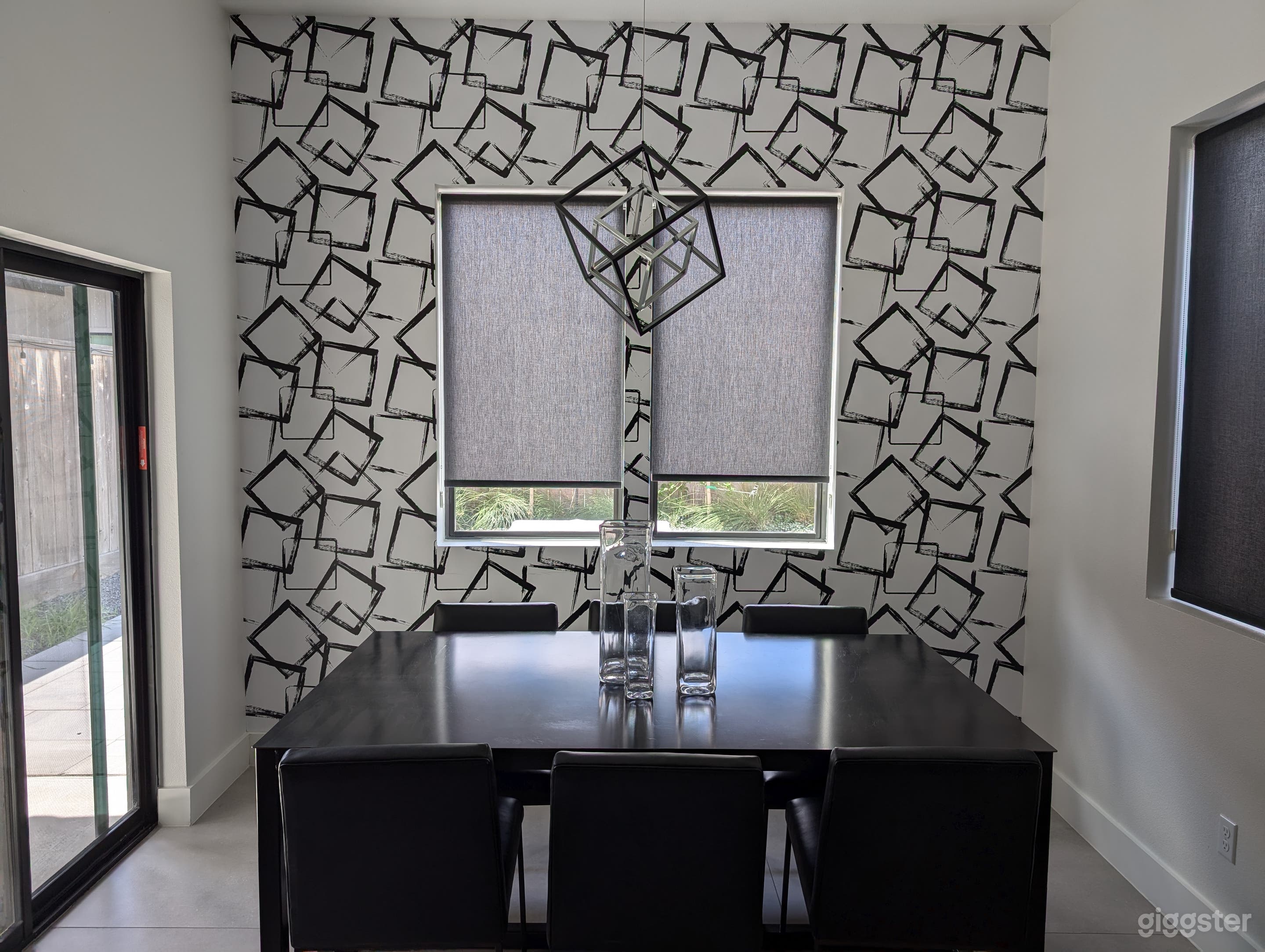 Graphic black and white wallpapered accent wall in the dining room from Houston-based Olivia + Poppy, with geometric cube LED light fixture. Table is custom distressed metal with black leather dining room chairs.