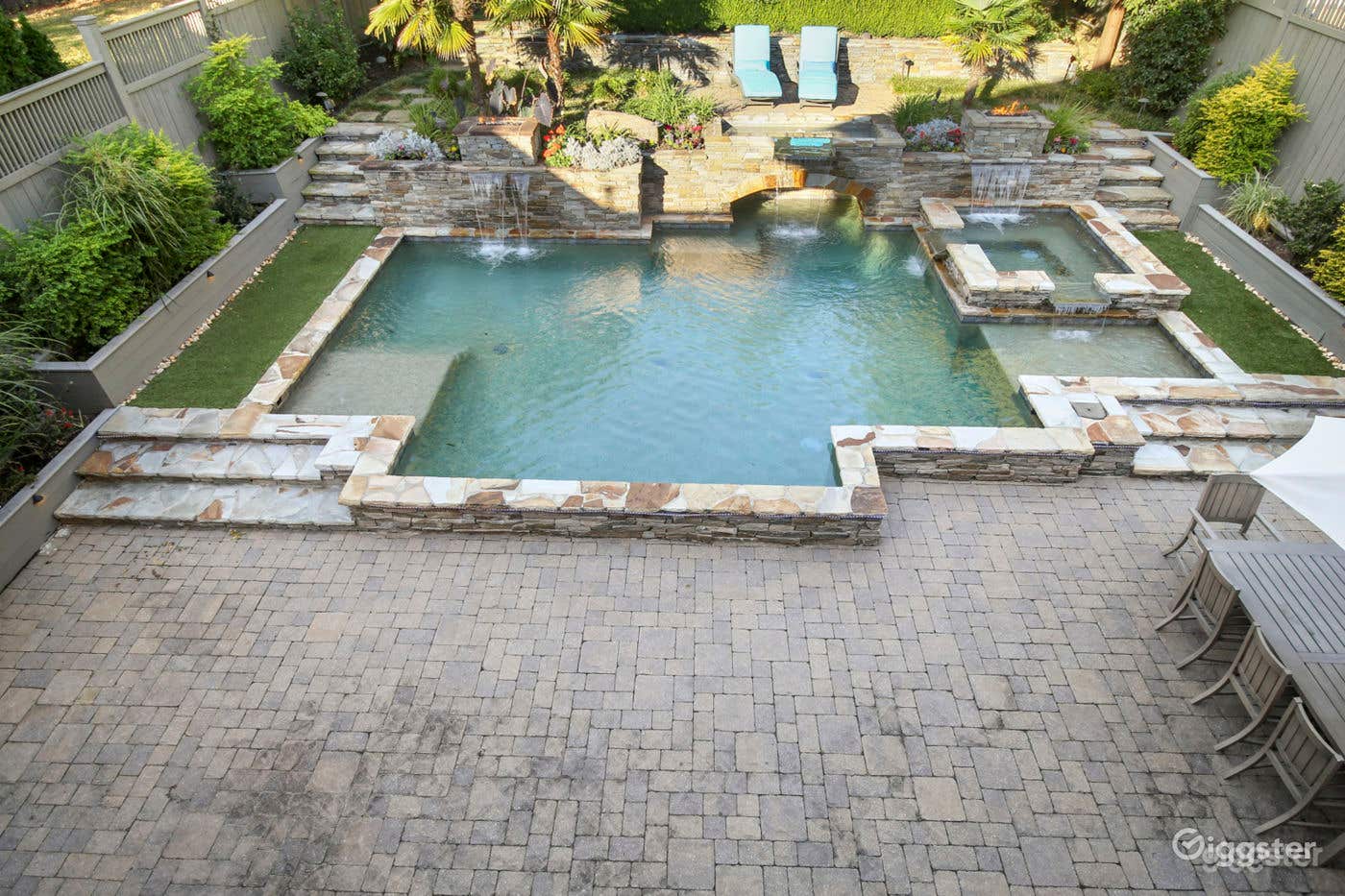 Saltwater pool encased in stone includes an inviting hot tub and two shallow side areas for lounging or swimming