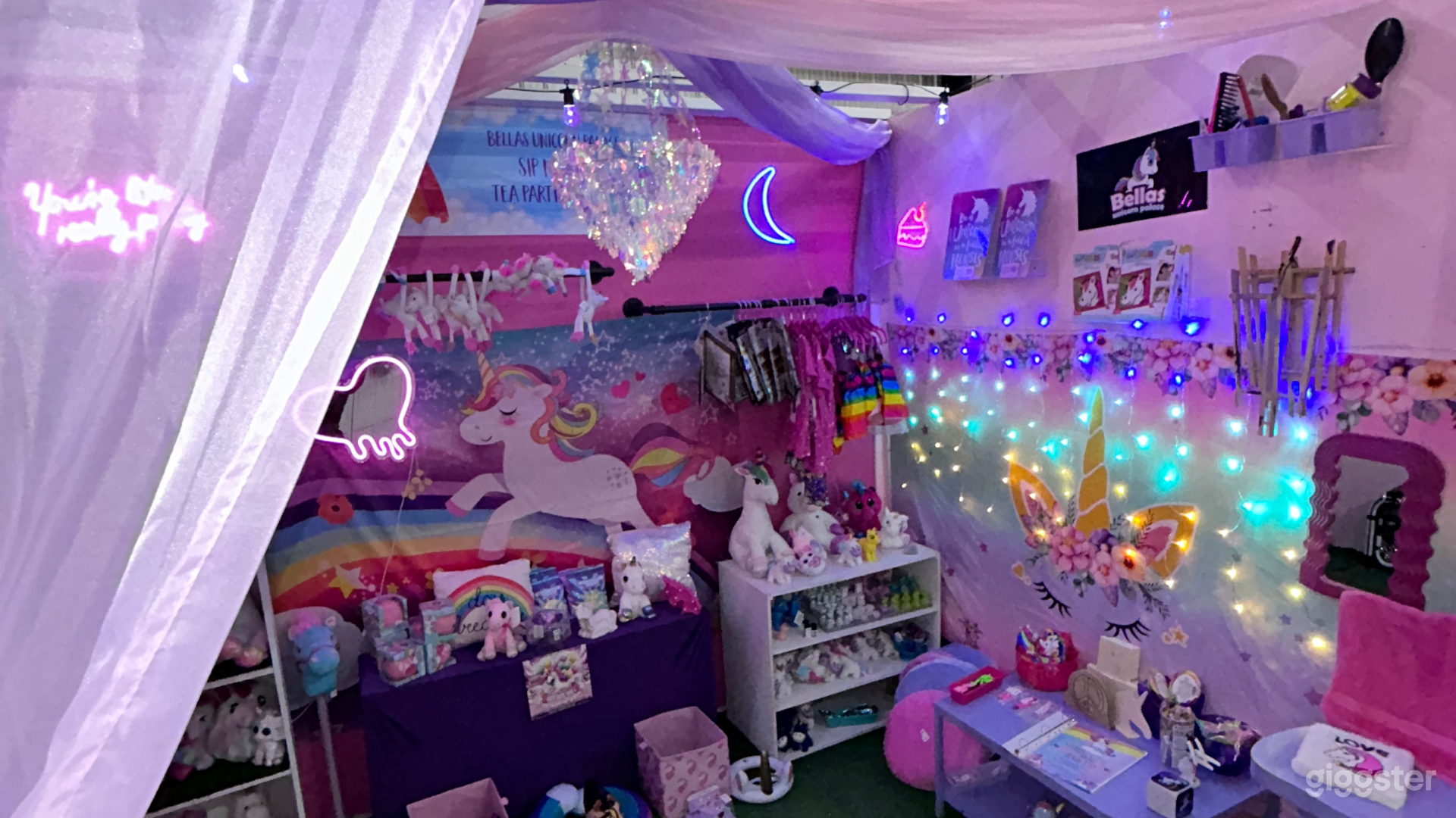 A wide shot of the unicorn-themed room showcasing various unicorn plush toys, rainbow-colored clothing, and themed accessories. The room is decorated with unicorn motifs on the walls and fairy lights hanging overhead, enhancing the magical feel