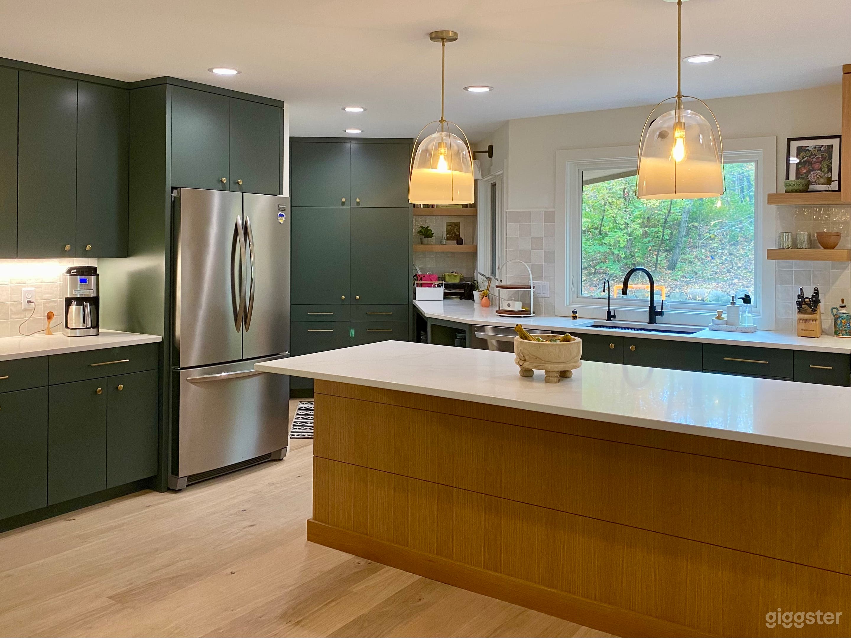 A light bright open concept kitchen. Green cabinets, white oak wood island, white quartz countertops, stainless steel appliances, white square tile backsplash and window over sink to private backyard. Scandinavian design inspired.