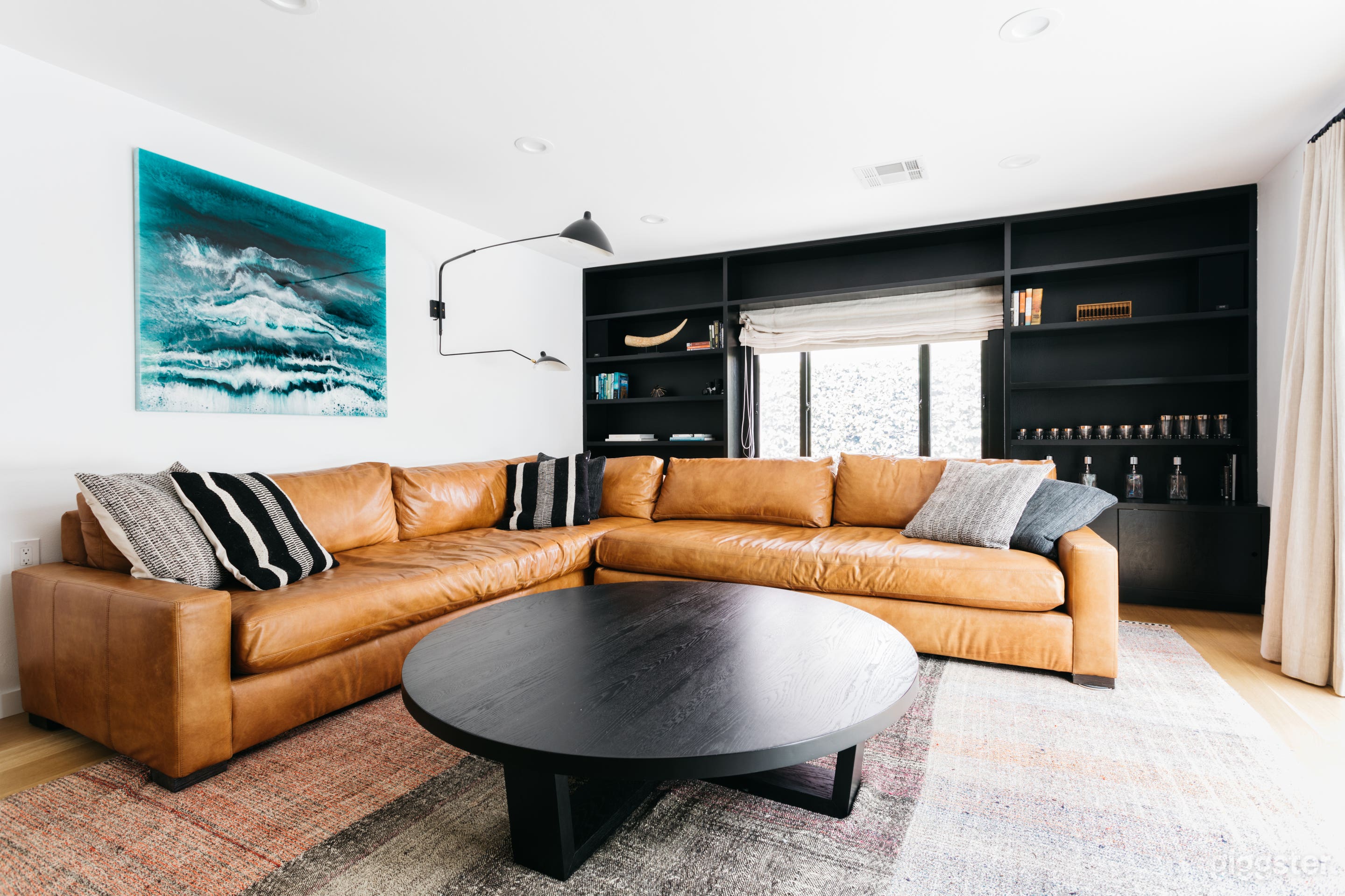 Large living room with large Restoration Hardware couch. Contrasting black built in shelves. Large set of doors open to backyard/garden. Original art.