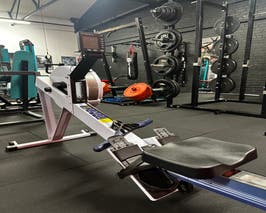  Concept 2 Rower with squat rack and black brick wall in the background 