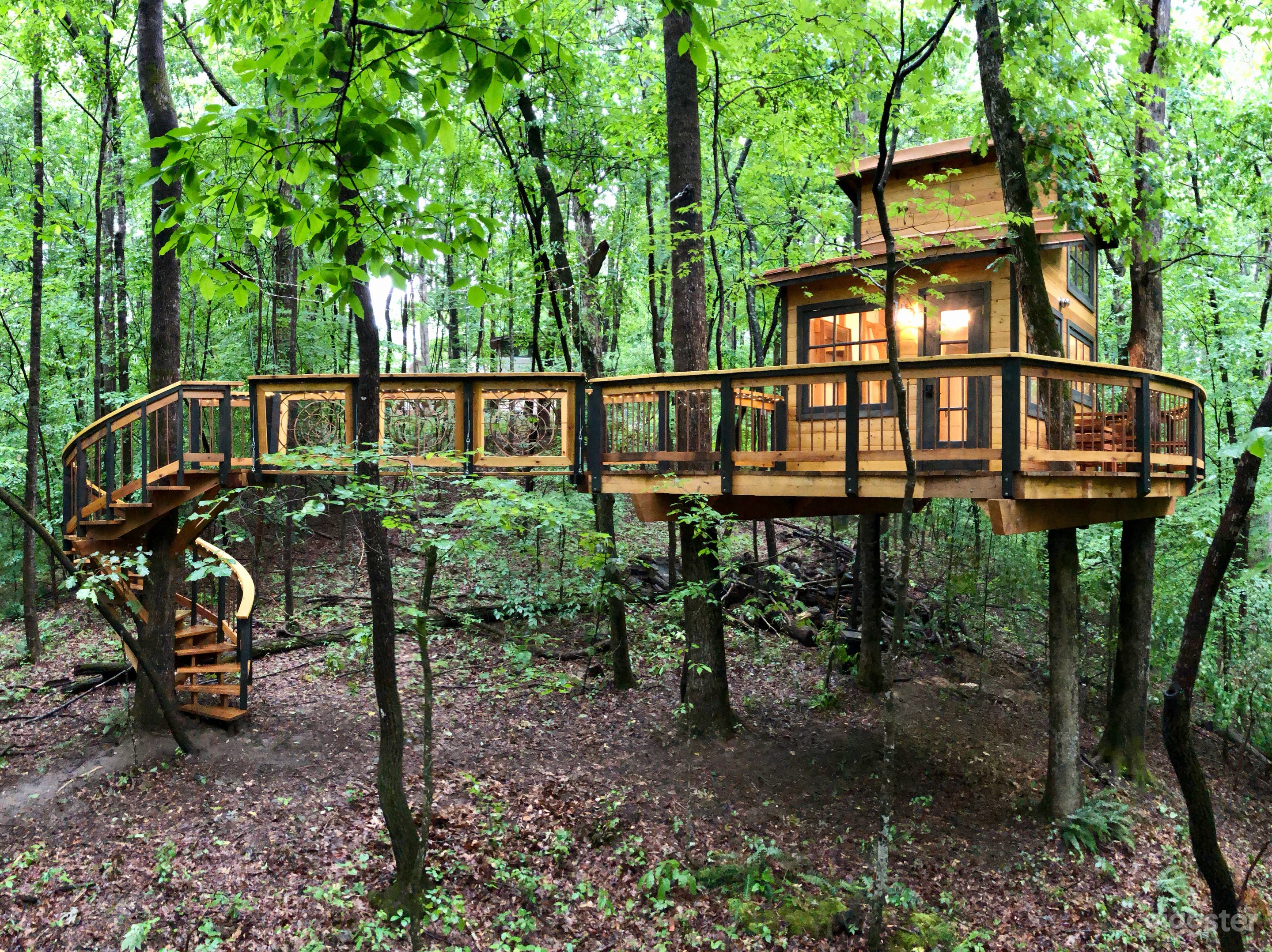 Spiral staircase, suspension bridge, and treehouse on its platform with large wraparound deck.