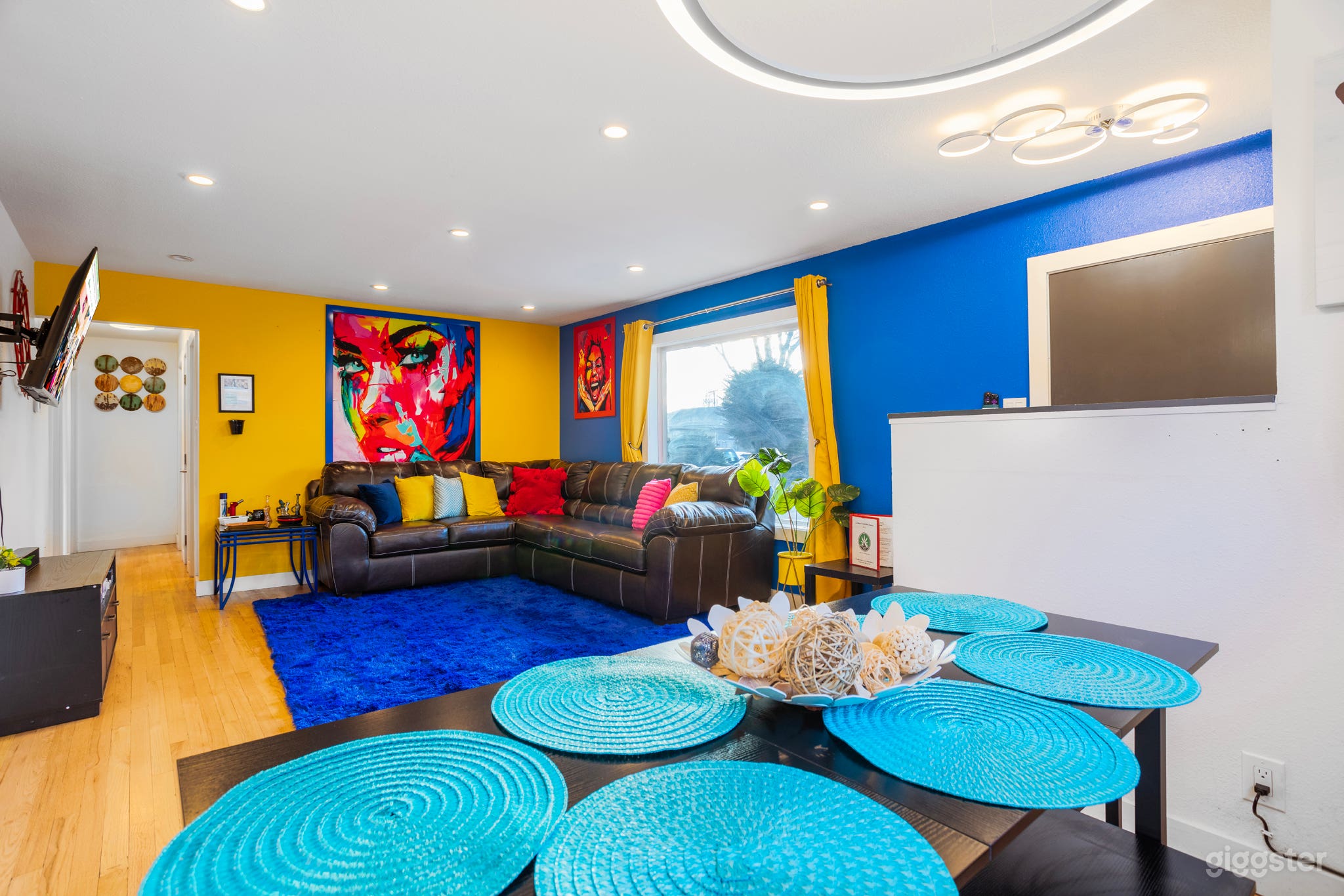 A living room adorned with colorful throw pillows against blue painted walls, complemented by a blue carpet and a TV for a cozy and vibrant gathering space.