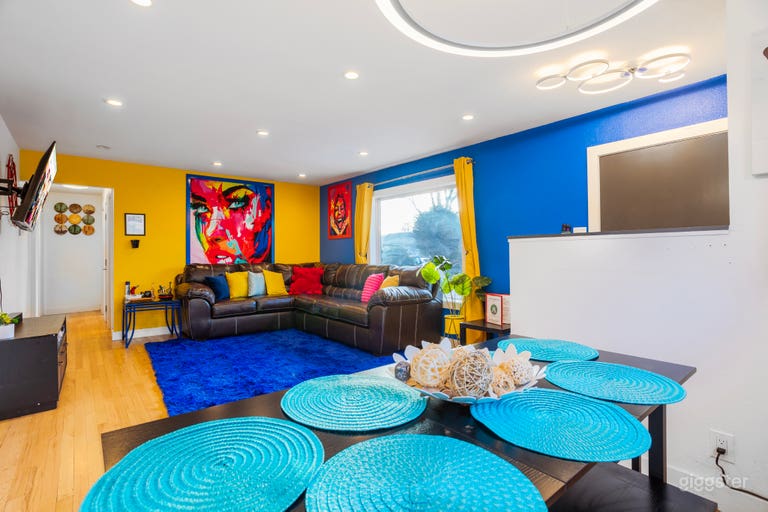  A living room adorned with colorful throw pillows against blue painted walls, complemented by a blue carpet and a TV for a cozy and vibrant gathering space. 