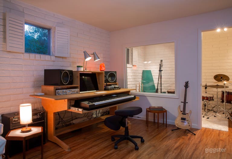  Studio with whitewashed brick walls, wood-look floors, a music workstation, and a sound booth. Features include a sleek keyboard, speakers, and mid-century modern Adrian Pearsall design. 