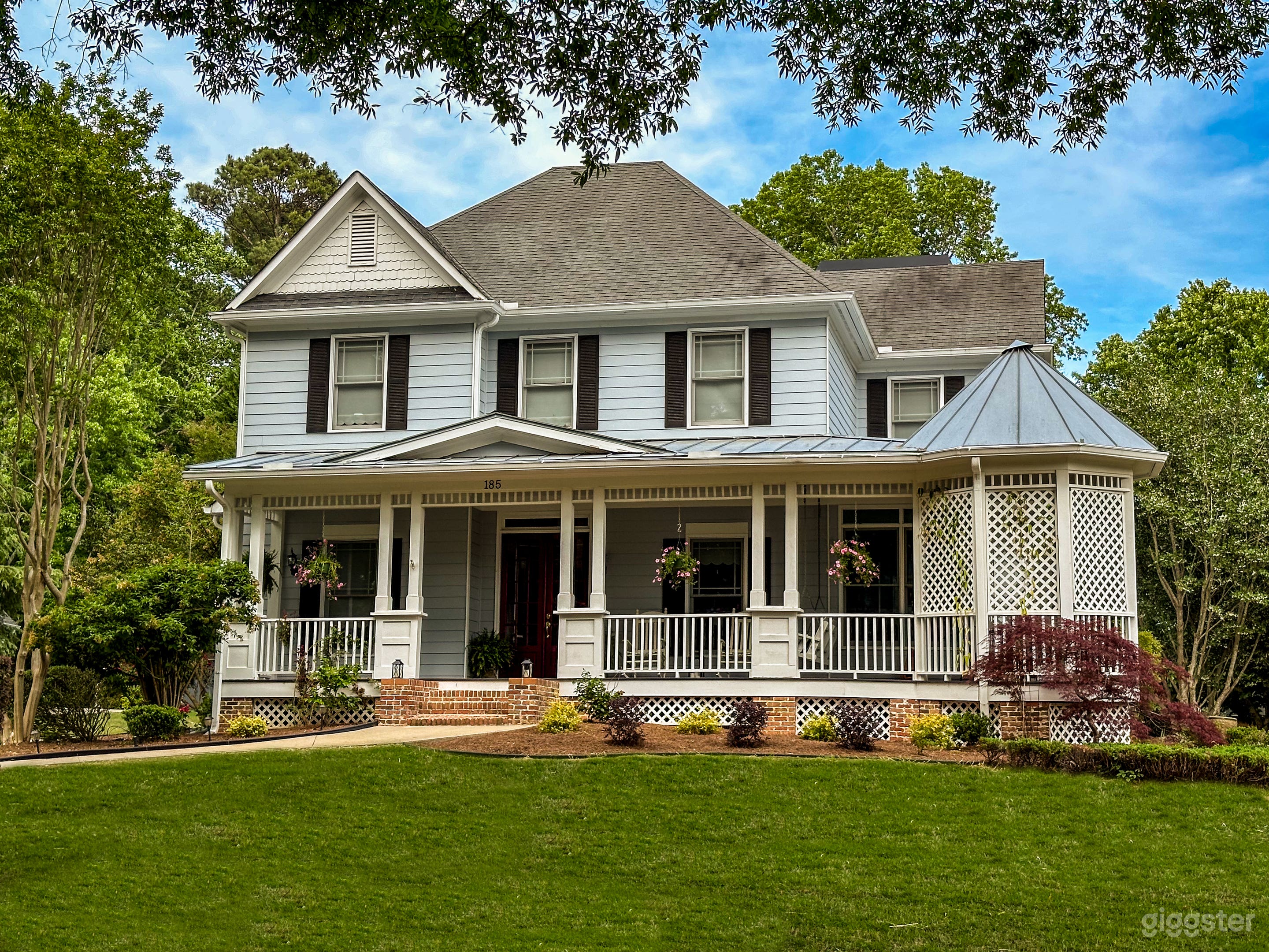 Large colonial-style home with light blue siding, red french doors, large porch, and beautiful grounds.
