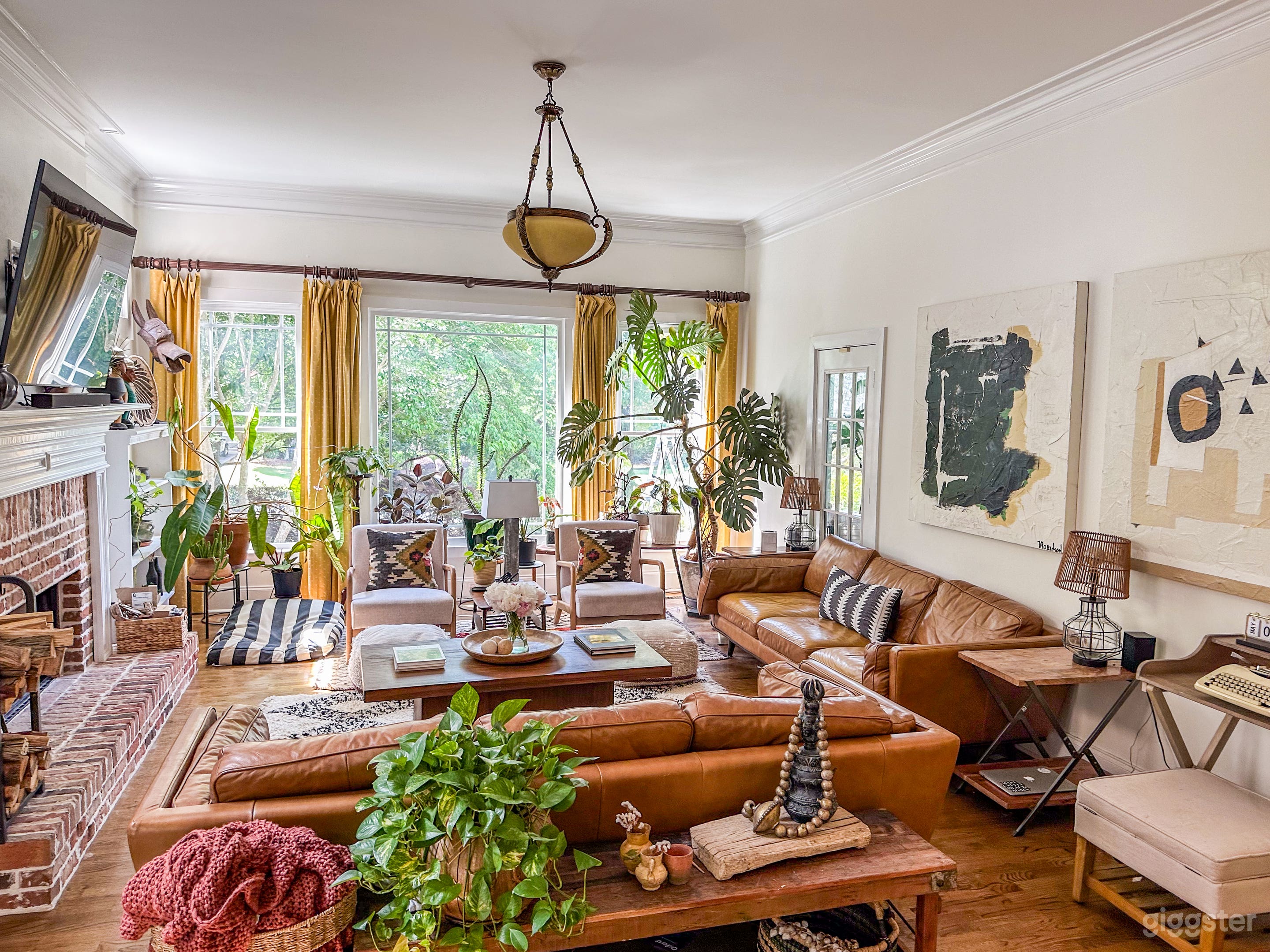 Epic living room with 65" TV, Fireplace with wide mantle, large plants, gold curtains, and sumptuous leather couches. 