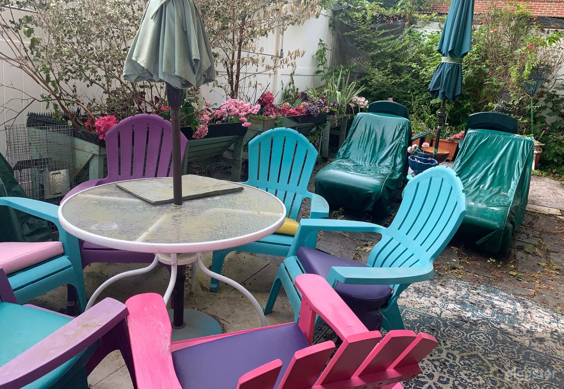 Full View of Back Yard In Bloom With Multiple Seating Areas - Table and Colorful Chairs, Dark Green Chaise Lounges and Dark Green Rocking Chairs
