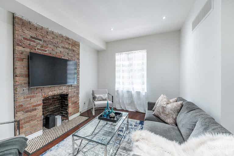  The living room has a large bright window and brick fireplace.  