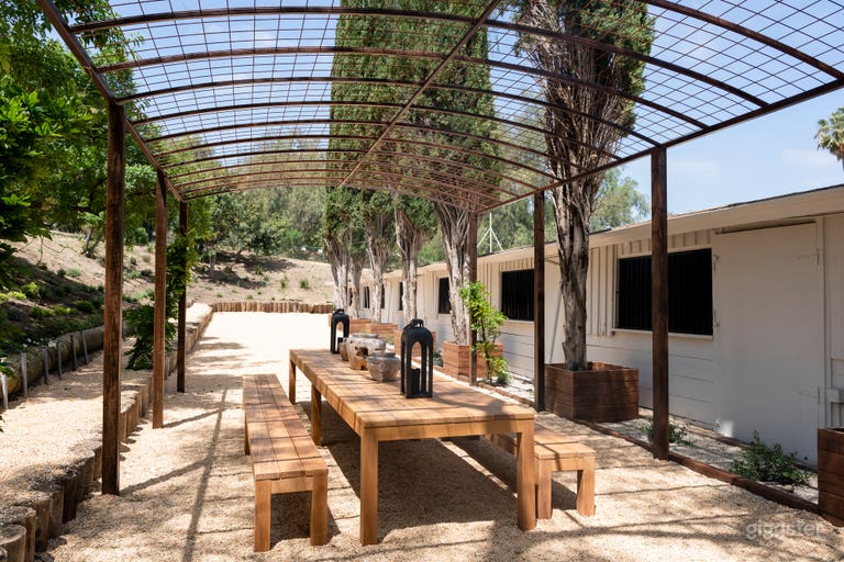  an outdoor communal area with designer Adirondack chairs and fire pits, custom iron arch with lights and mature trees and a vintage oak communal table 