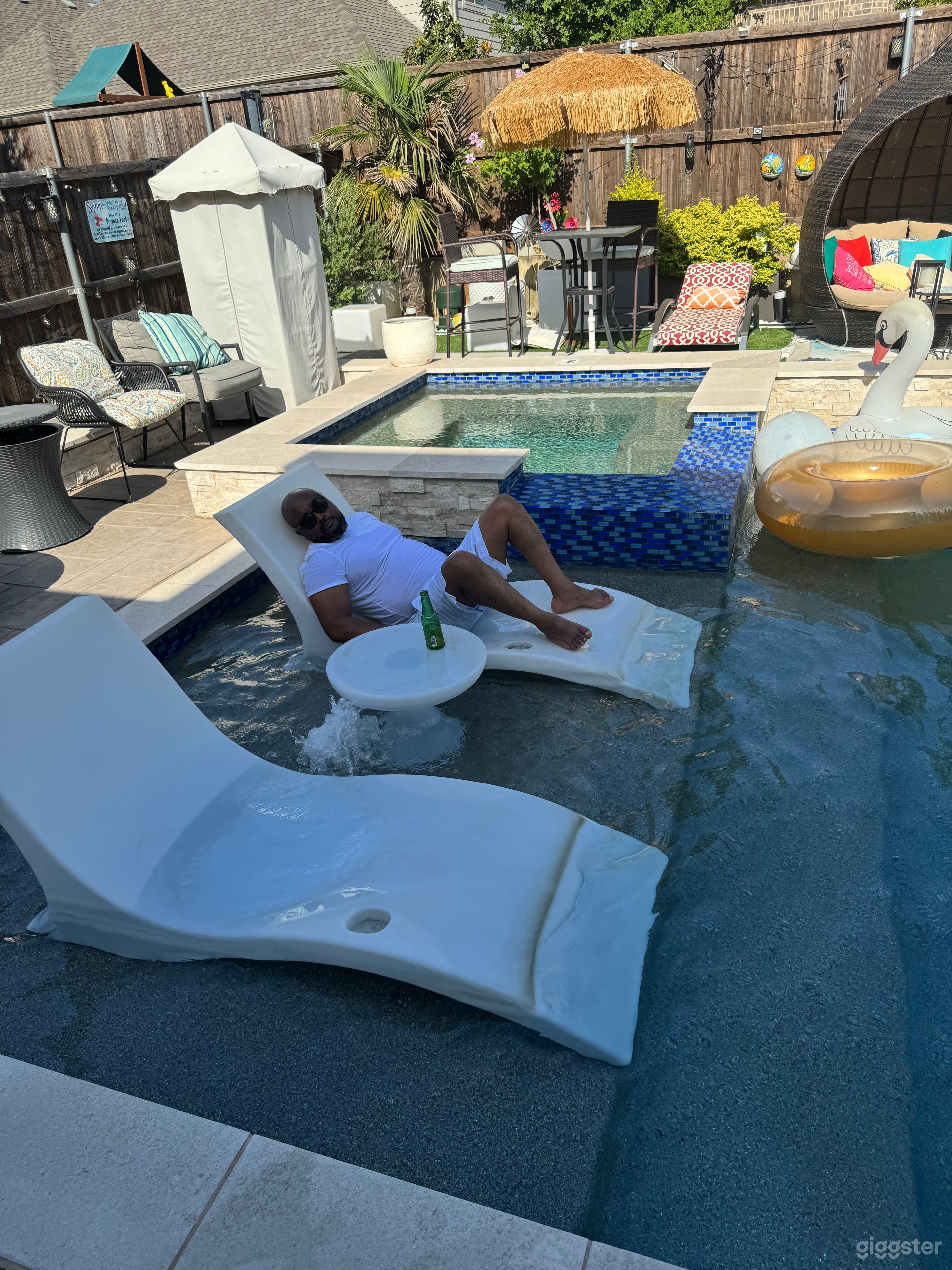 The image features a luxurious outdoor pool area with a variety of amenities designed for relaxation and entertainment. Notable items include:

- A spa with blue mosaic tile accents.
- Pool lounges positioned in shallow water for in-pool relaxation.
-