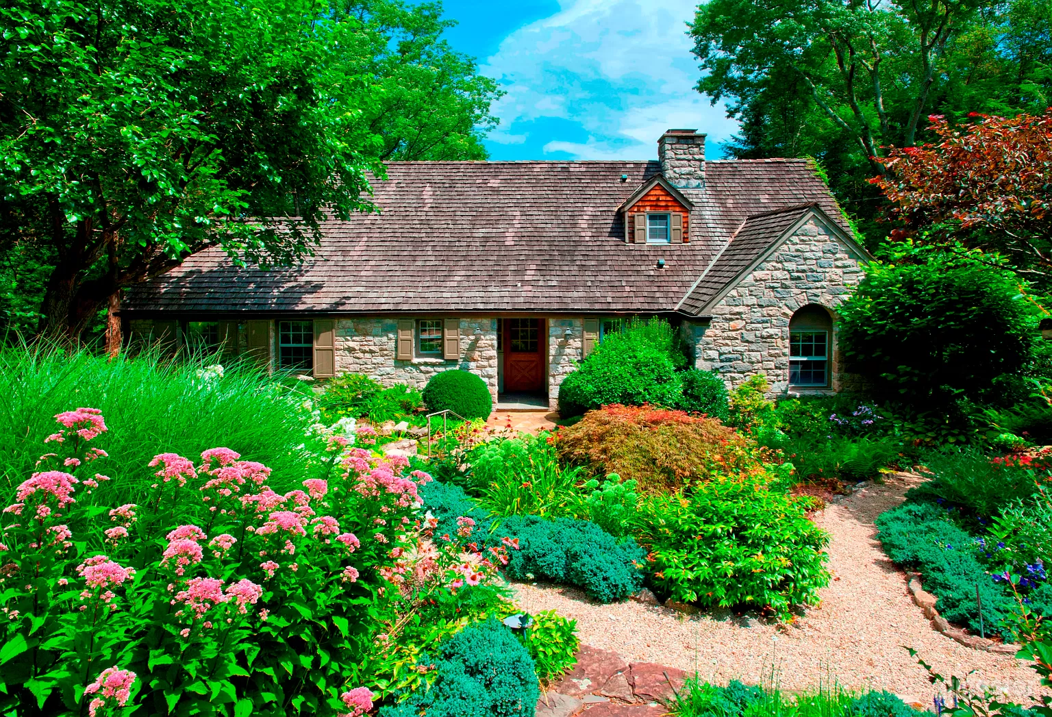 Front of stone cottage nestled within an expansive garden that wraps around the right side.
