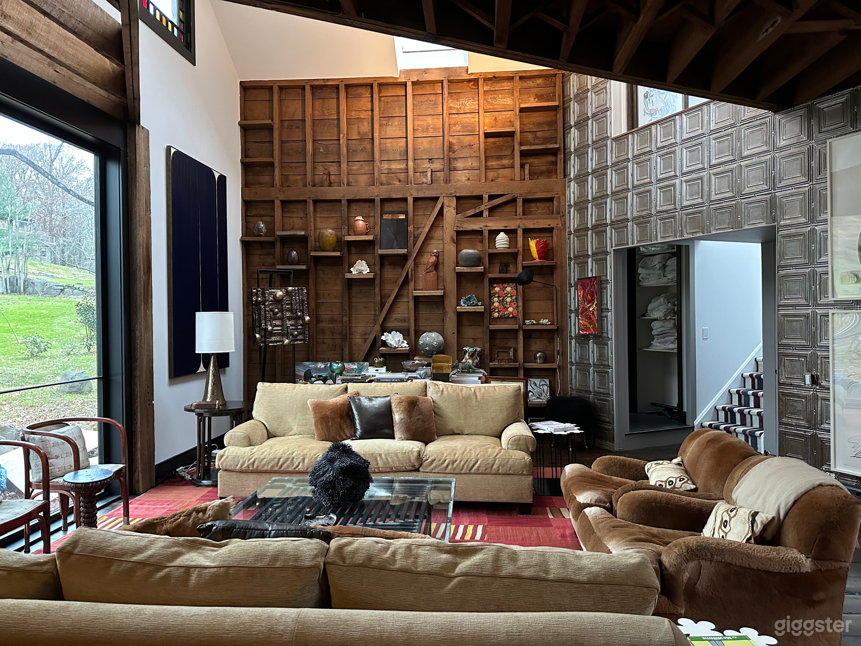 Double-height living room, with 2 wood walls and 1 pressed tin wall and sideboard wood flooring, decorated with works of art and chic furniture. 