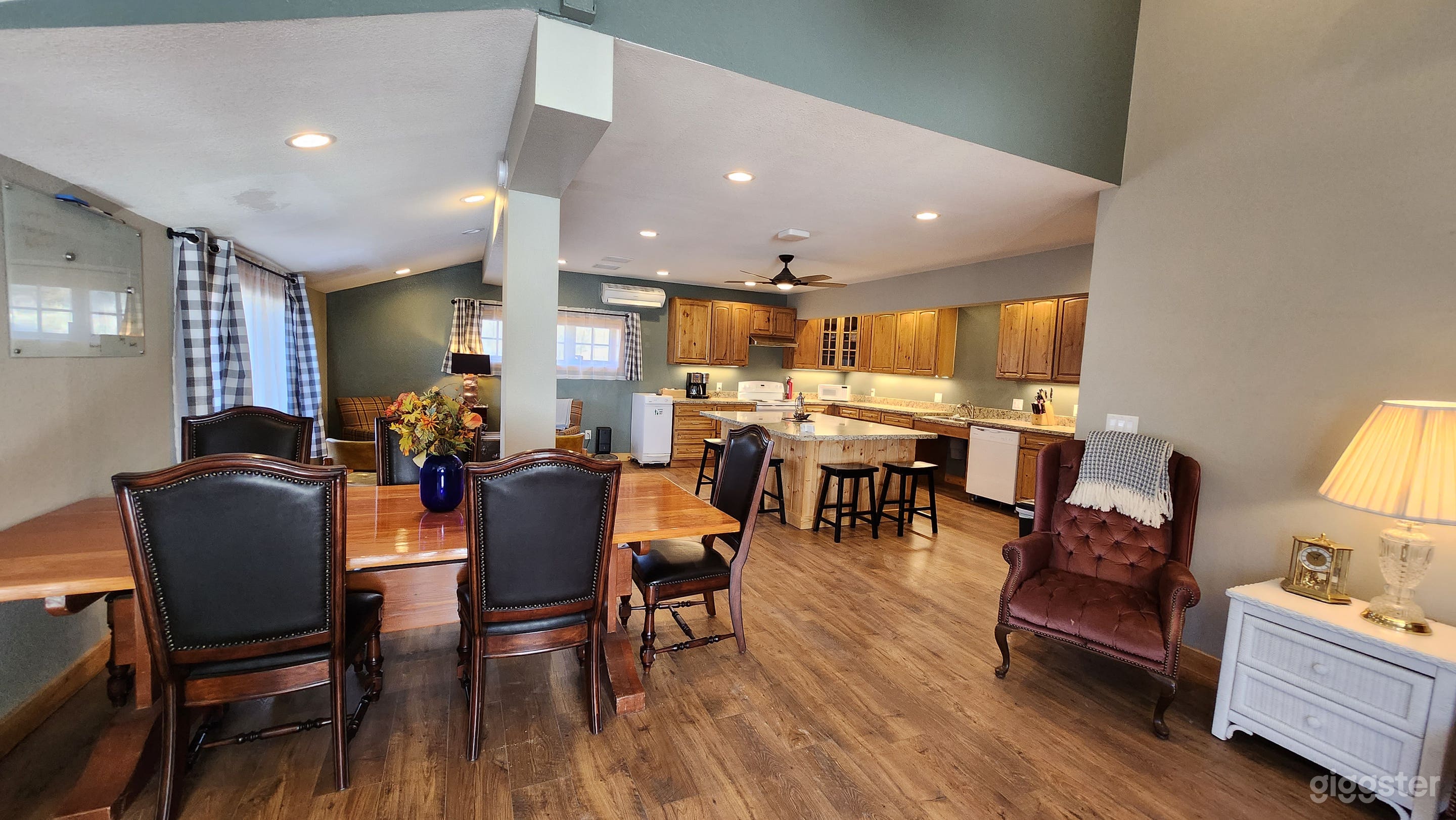A cozy, well-appointed kitchen and dining area boasting wooden furniture and cabinetry, accented by warm lighting, earthy tones, and homely decor. Natural light filters through gingham curtains, adding to the inviting ambiance of your interior.