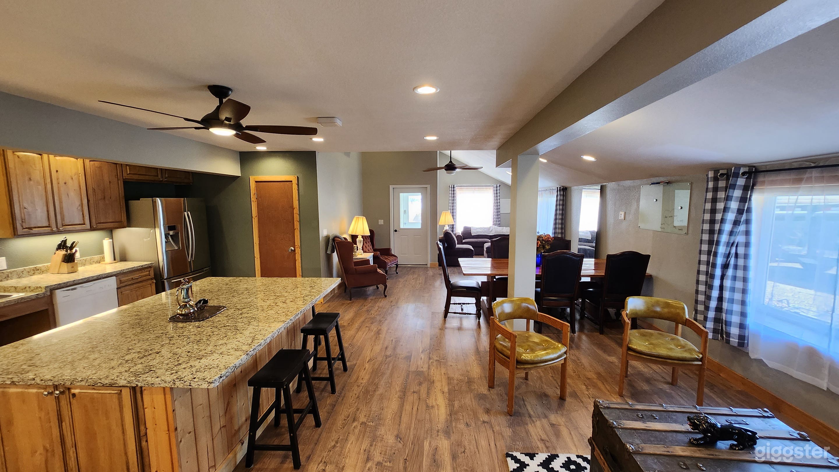 A spacious and well-lit open-concept space, featuring a kitchen and a dining area seamlessly transitioning into a cozy living room. The kitchen has modern, wooden cabinets, a large island with granite countertops.