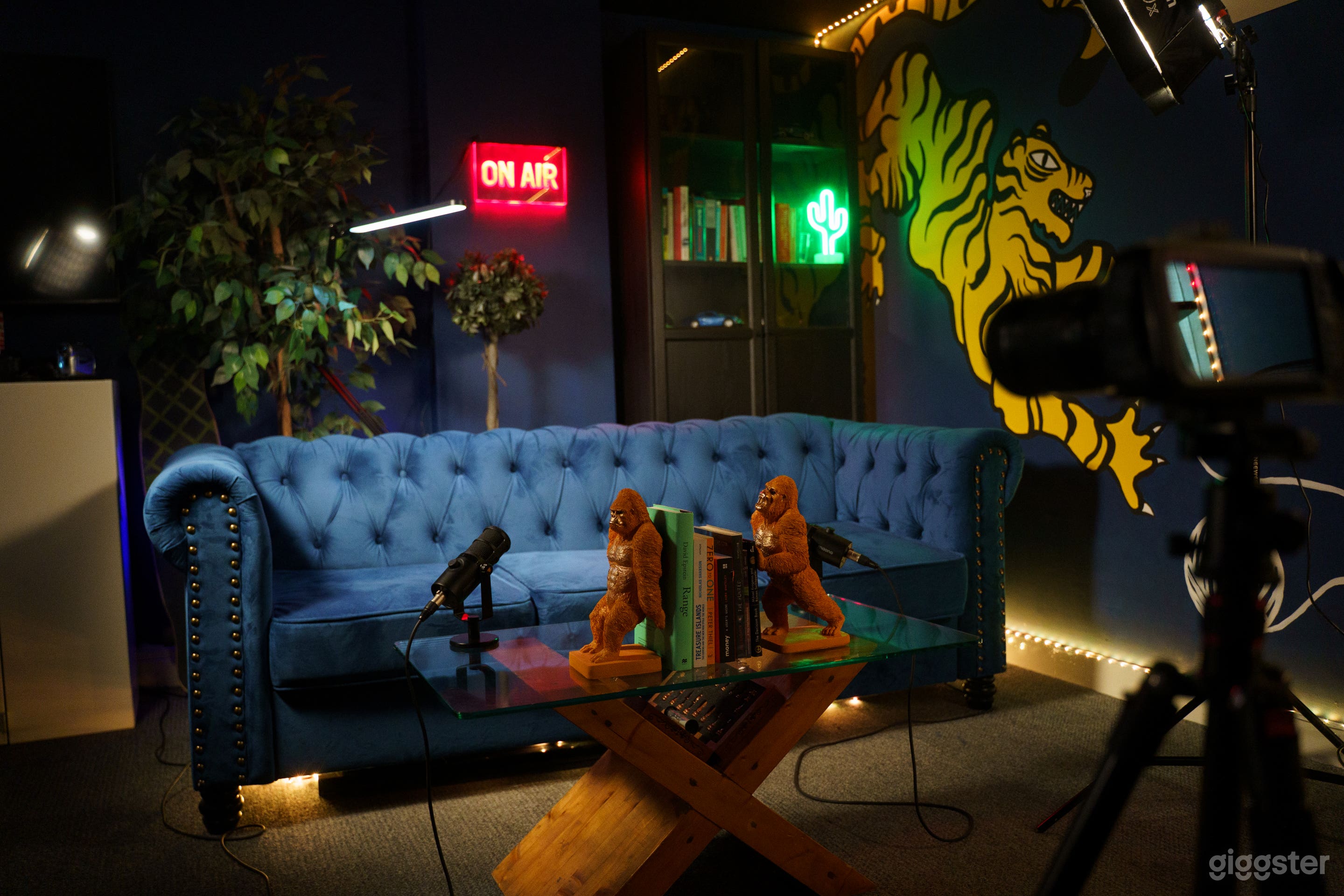 Our bold setup features a plush velvet sofa, dual professional mics, a custom-styled glass coffee table, and ambient LED lighting. The perfect scene for podcast episodes, interviews, or content that demands attention.