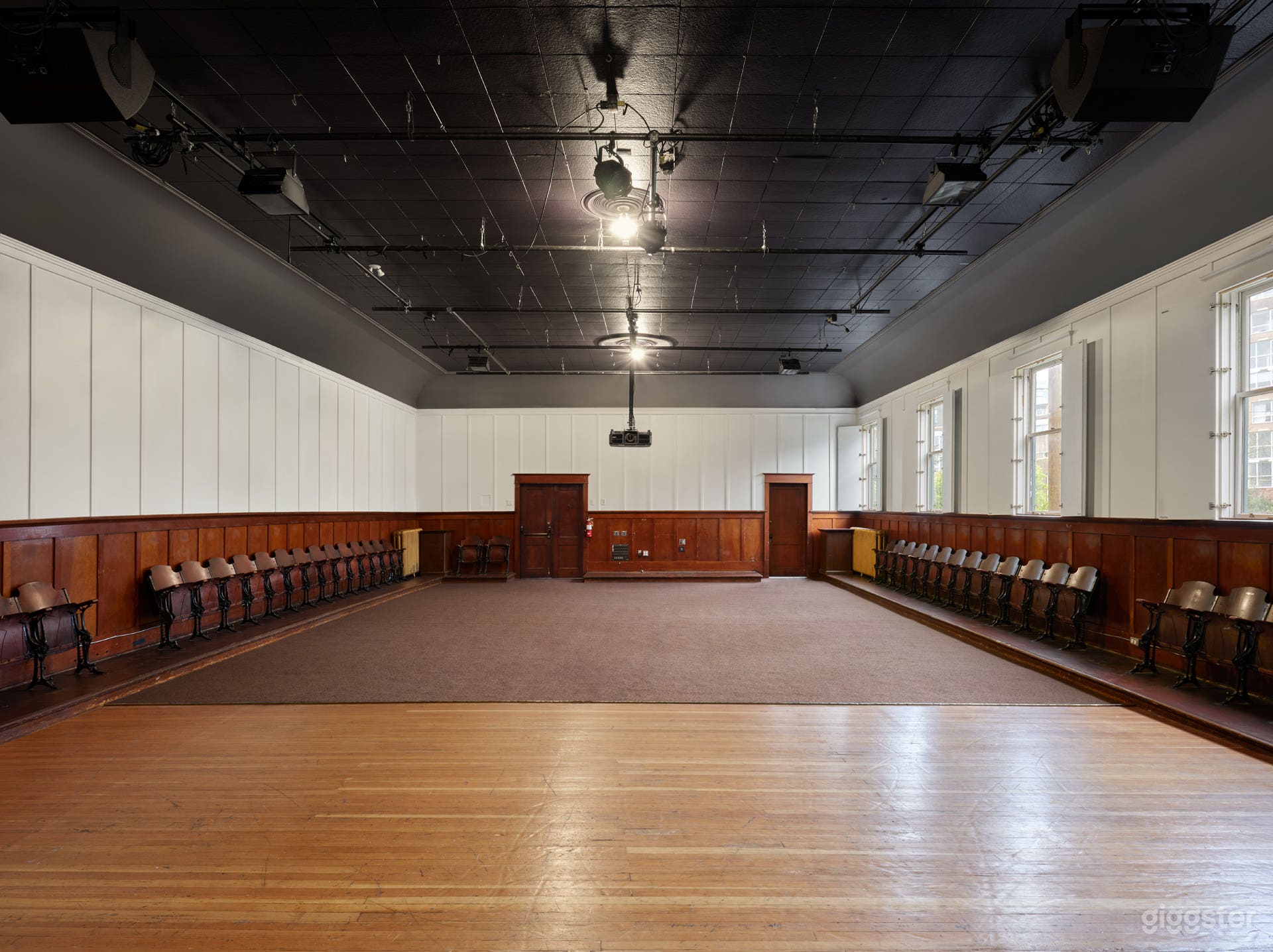 Interior of the hall featuring the hardwood stage, natural light streaming through open windows, and the hall’s warm, vintage character on full display.