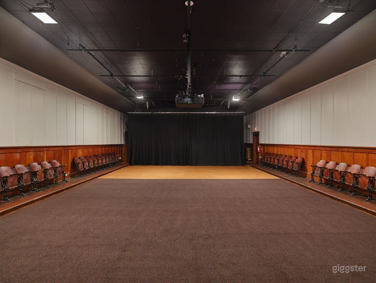  Interior of the hall with the hardwood stage exposed, windows closed, and the hall’s warm, vintage character highlighted by soft, ambient light. 