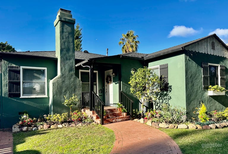  Front yard features grassy green lawn, leafy evergreen foliage, and flowering plants. Black painted wood shutters, porch railing and gutters accent this green and white cottage palette. 