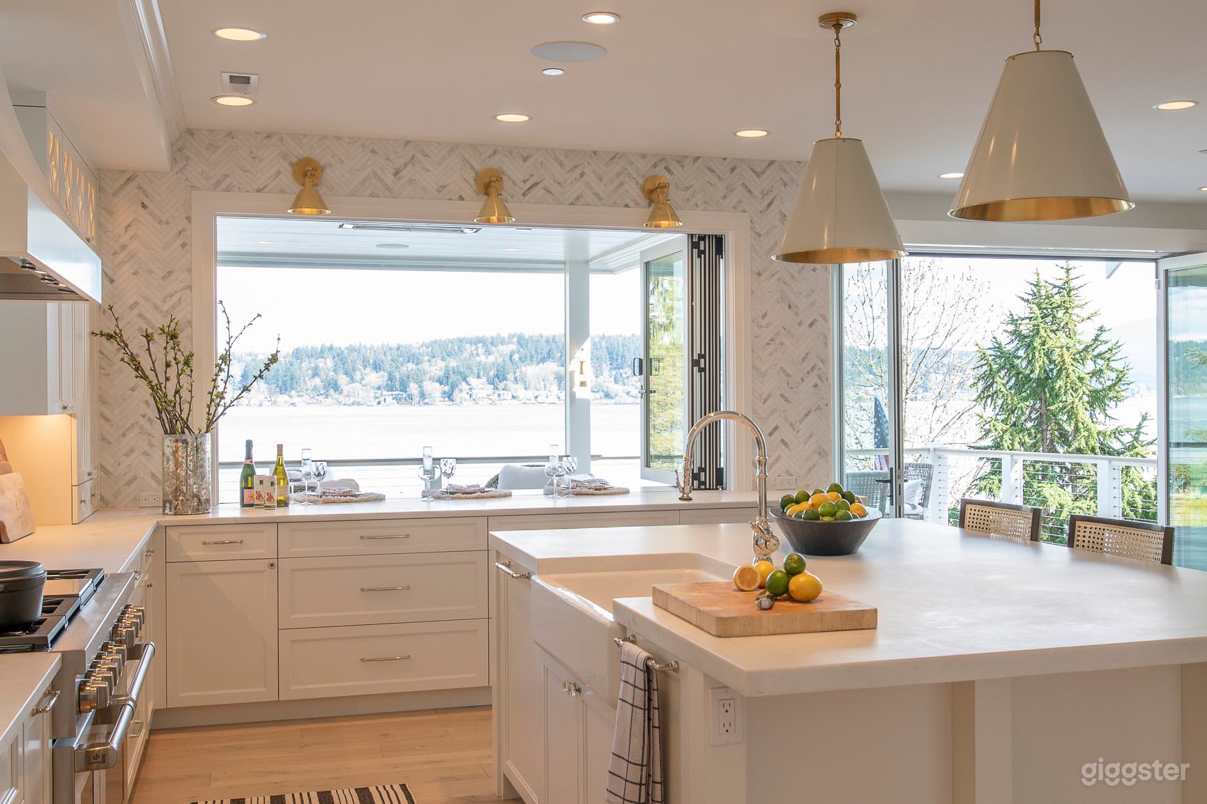Chef's kitchen in white marble with marble herringbone backsplash and fully opening doors and windows to view deck