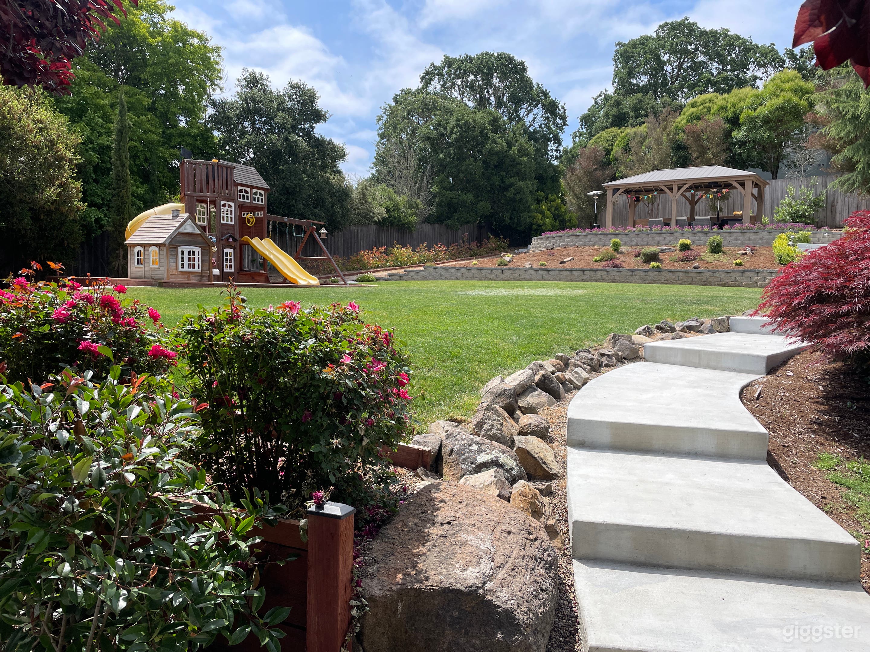Architectural white washed concrete steps  with natural stone border leading to lush green lawn with play structure. Gazebo in the background 