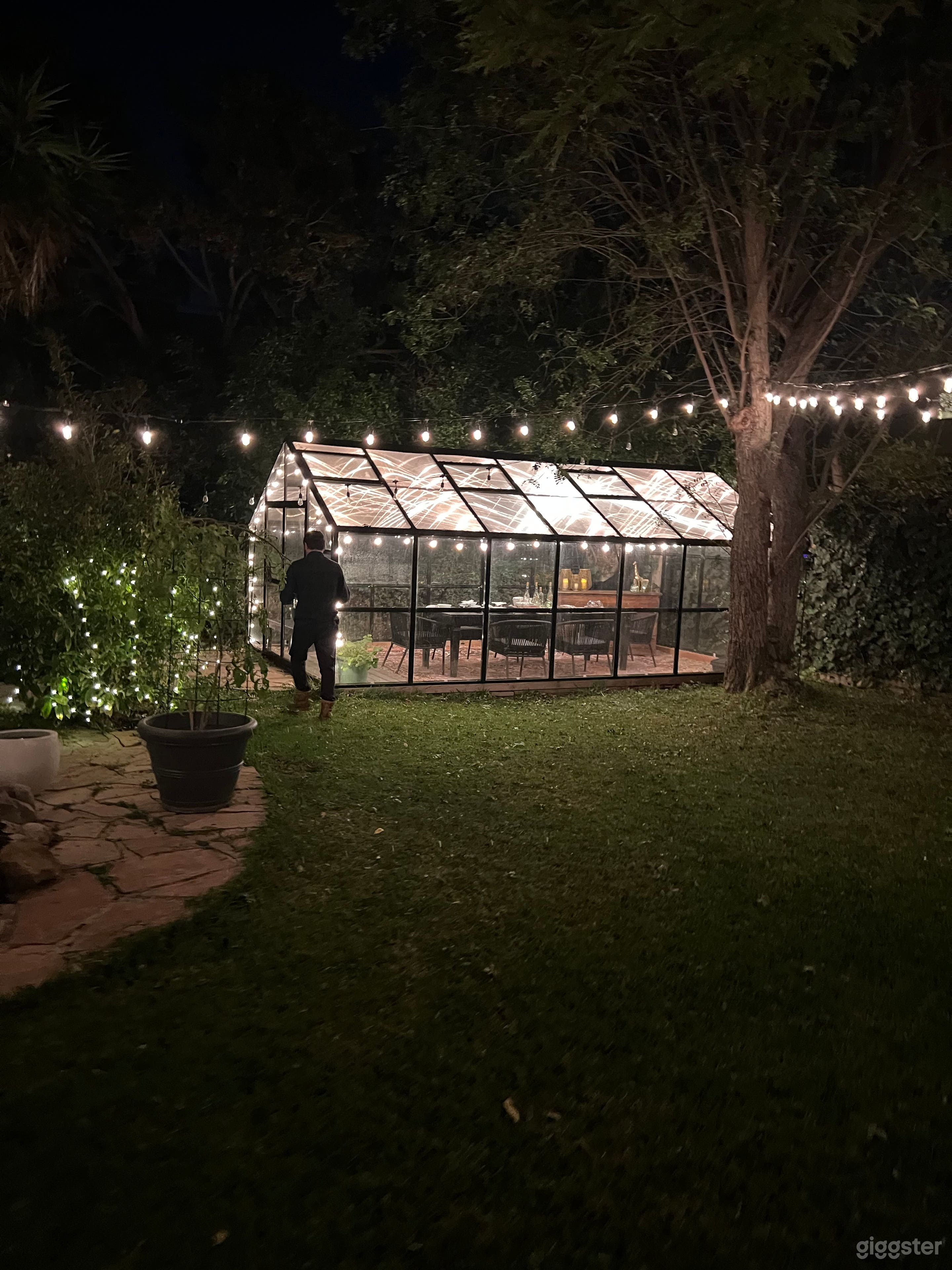 Romantic glass-walled greenhouse surrounded by string lights inside and out