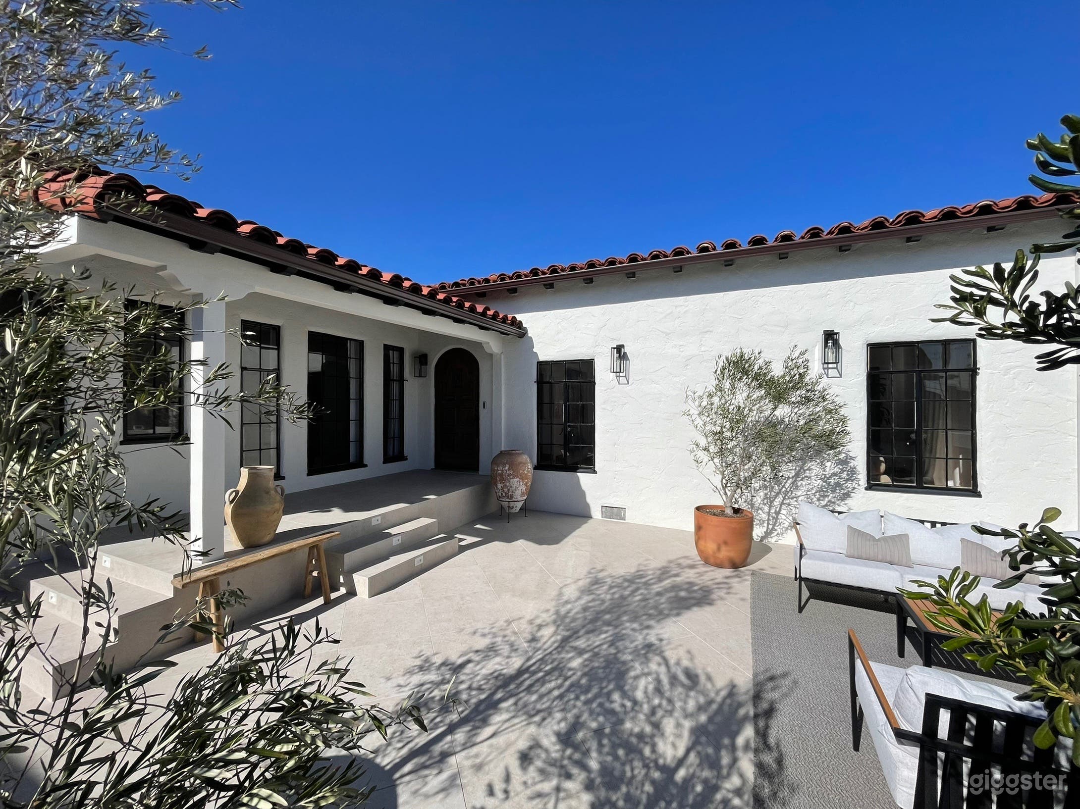 A Bright Mediterranean Patio with a Large Outdoor fireplace, vintage pots and olive trees. 