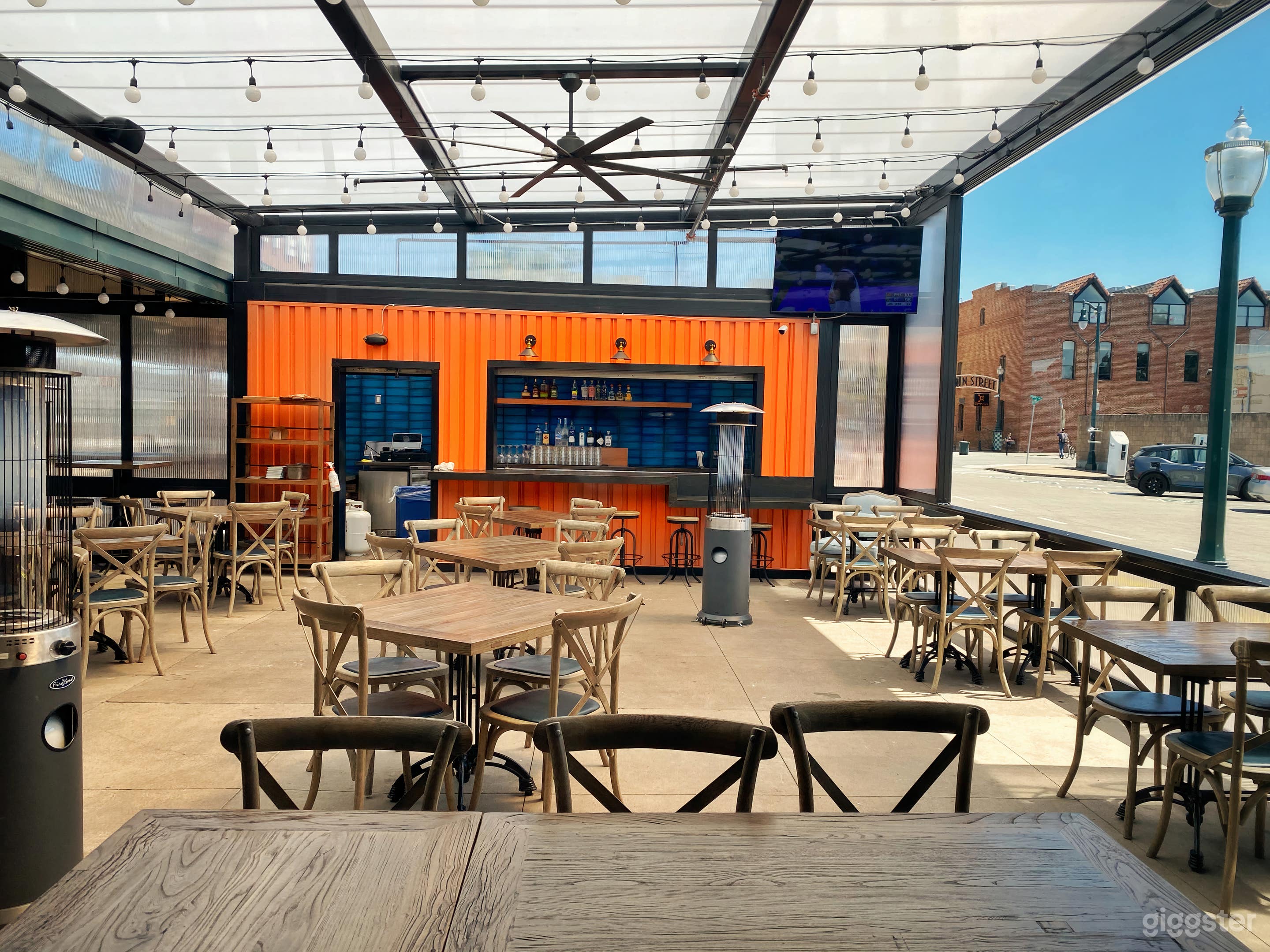 Cozy and inviting outdoor patio with a bar. Heated by fire pits, and wall-sized windows open up for circulation. String lights for ambience. Large communal tables and booth-style seating, and traditional table seating.