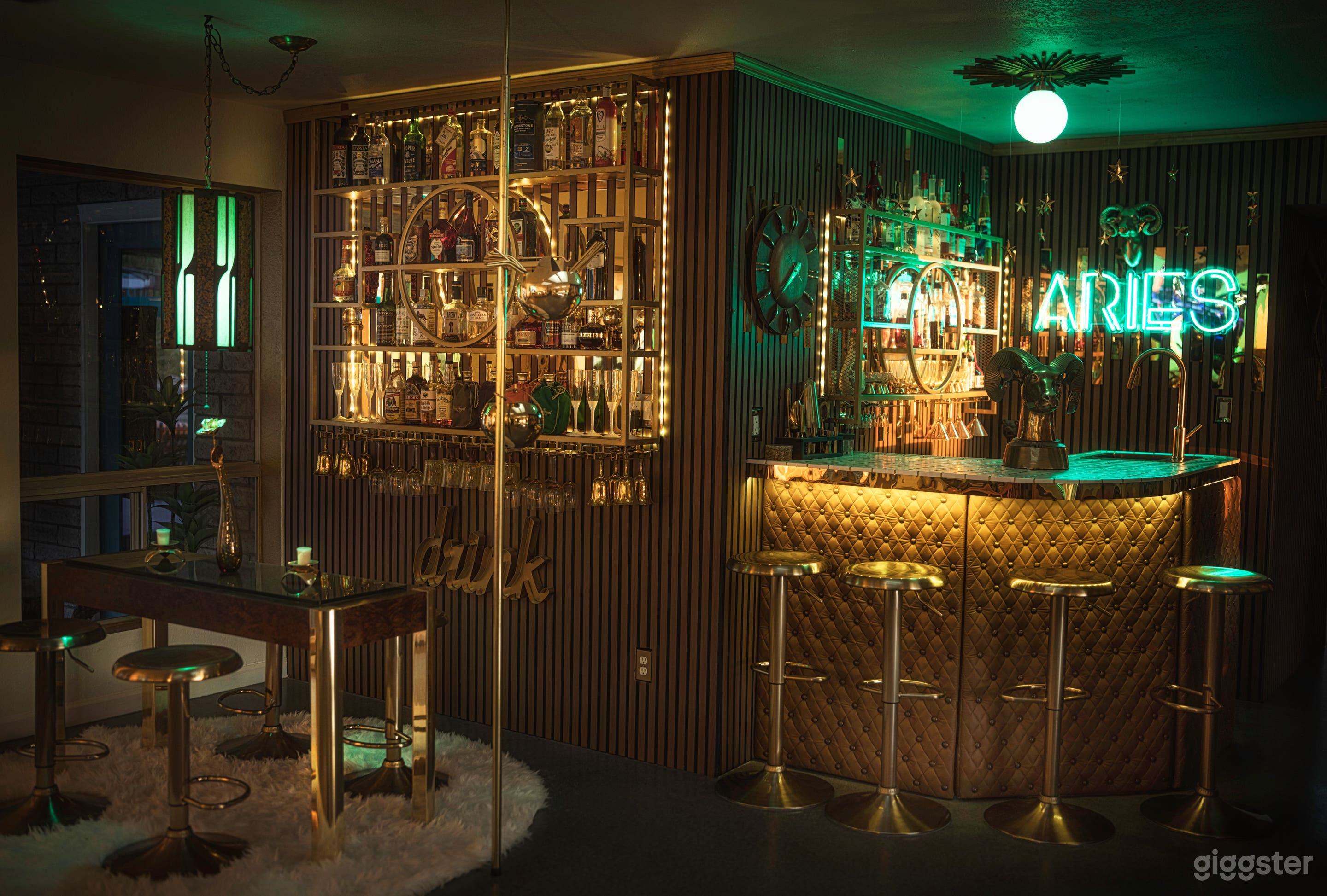 The Aries Bar is a moody midcentury lounge featuring warm wood paneling, a tufted gold bar, glowing neon, mirrored liquor wall, and tension pole. A vintage seating area completes the cinematic vibe—perfect for cocktail scenes, retro shoots, and nightlife. 